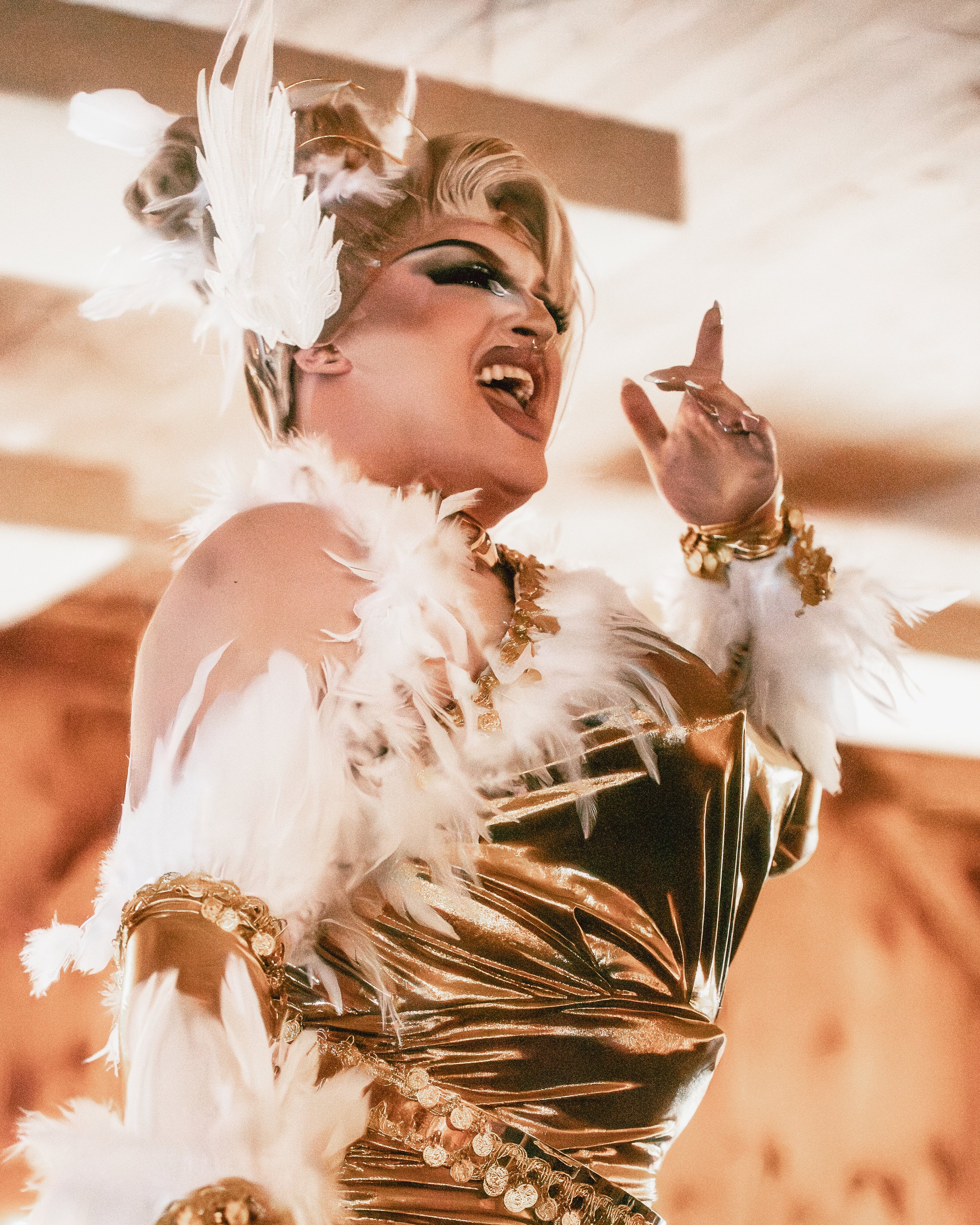 A performer dressed in elaborate gold and white costume with feathers, singing passionately on stage.