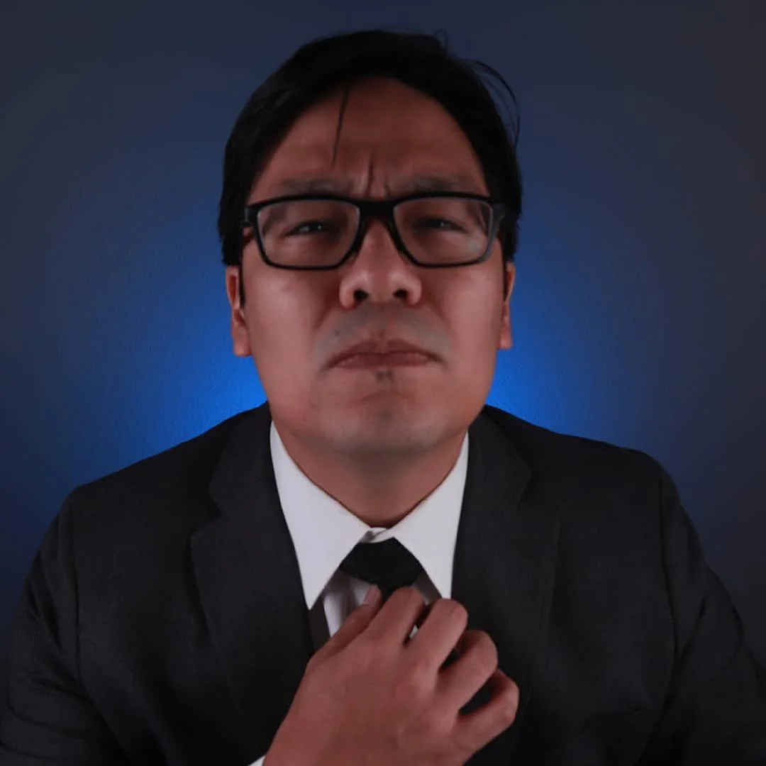Man in black suit adjusting black tie, wearing glasses, with an intense facial expression, against a dark blue background.