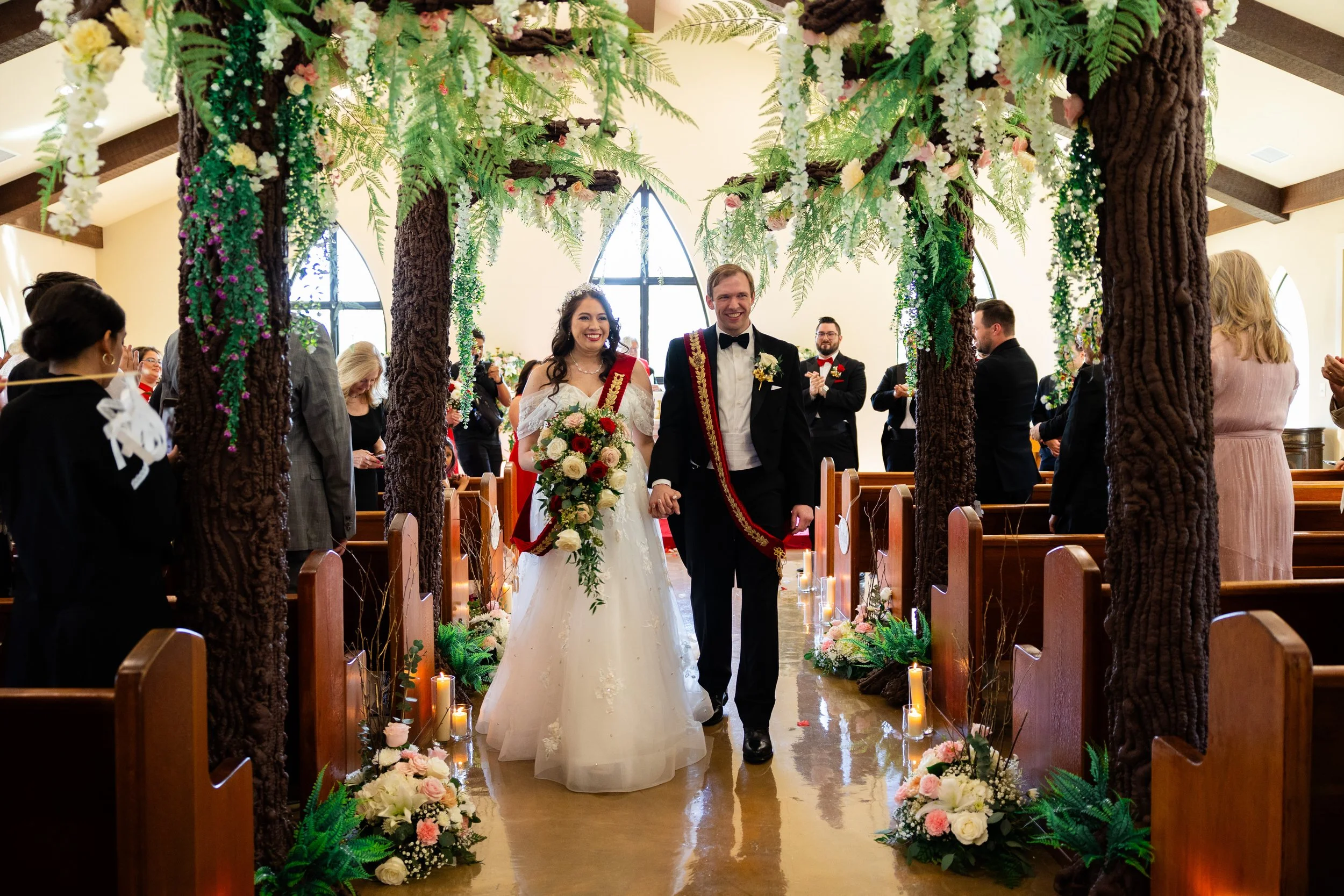 A bride and groom walking down the aisle in a church decorated with flowers and candles, surrounded by guests celebrating their wedding.