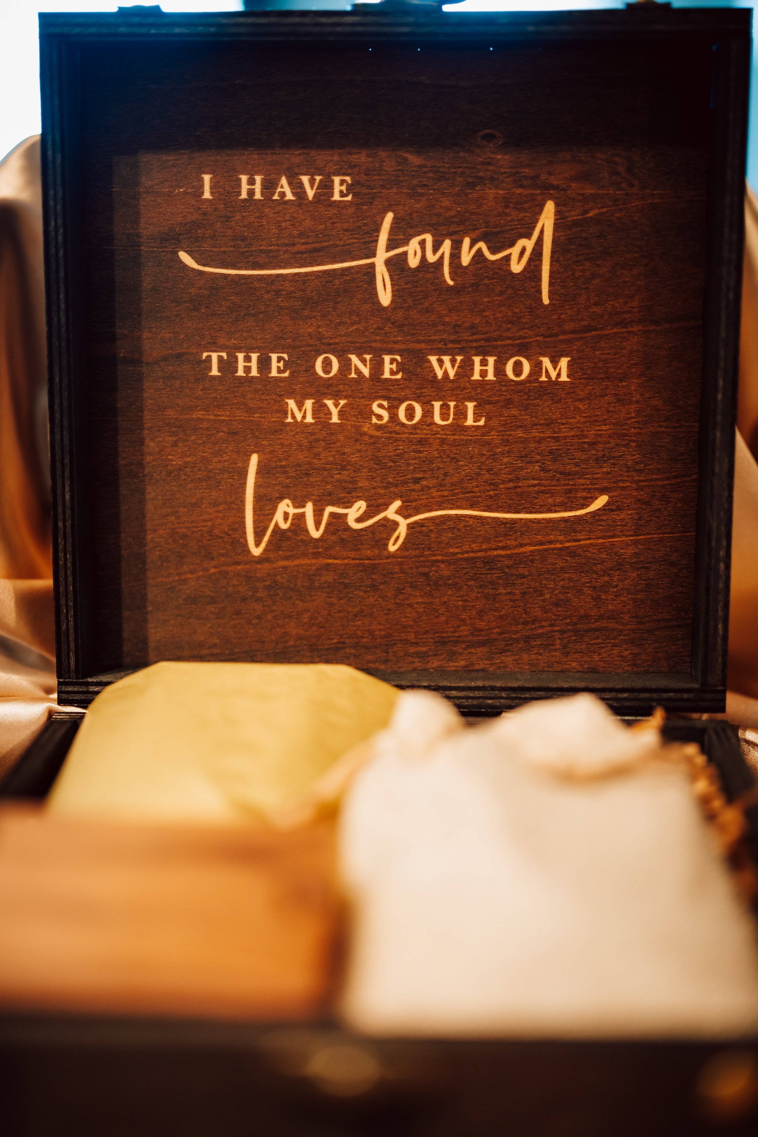 A wooden box with a quote that reads, 'I have found the one whom my soul loves.' The box contains a candle and a white flower.