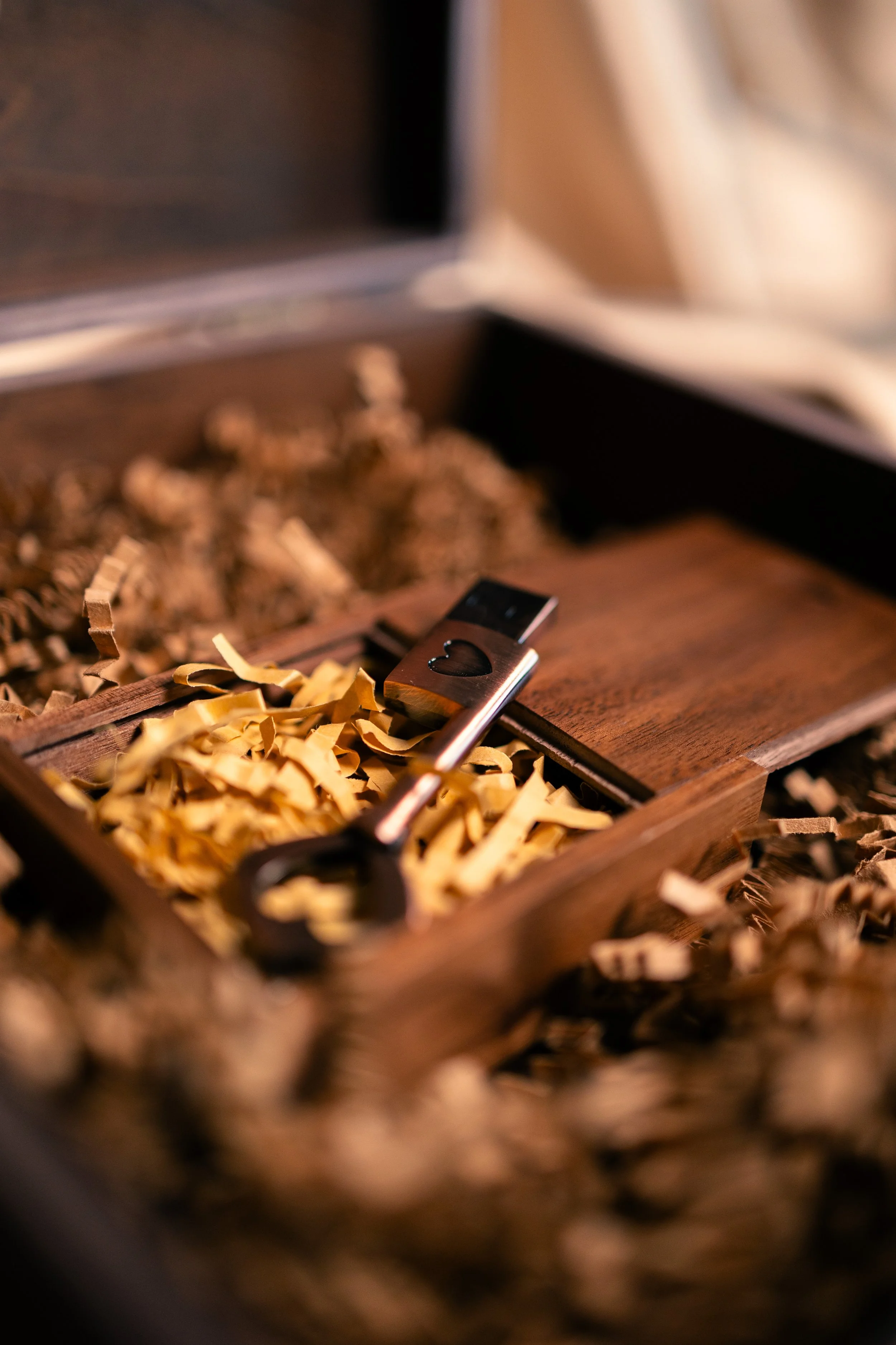A wooden box with shredded paper inside, a metal key with a heart-shaped cutout on one end resting among the paper.