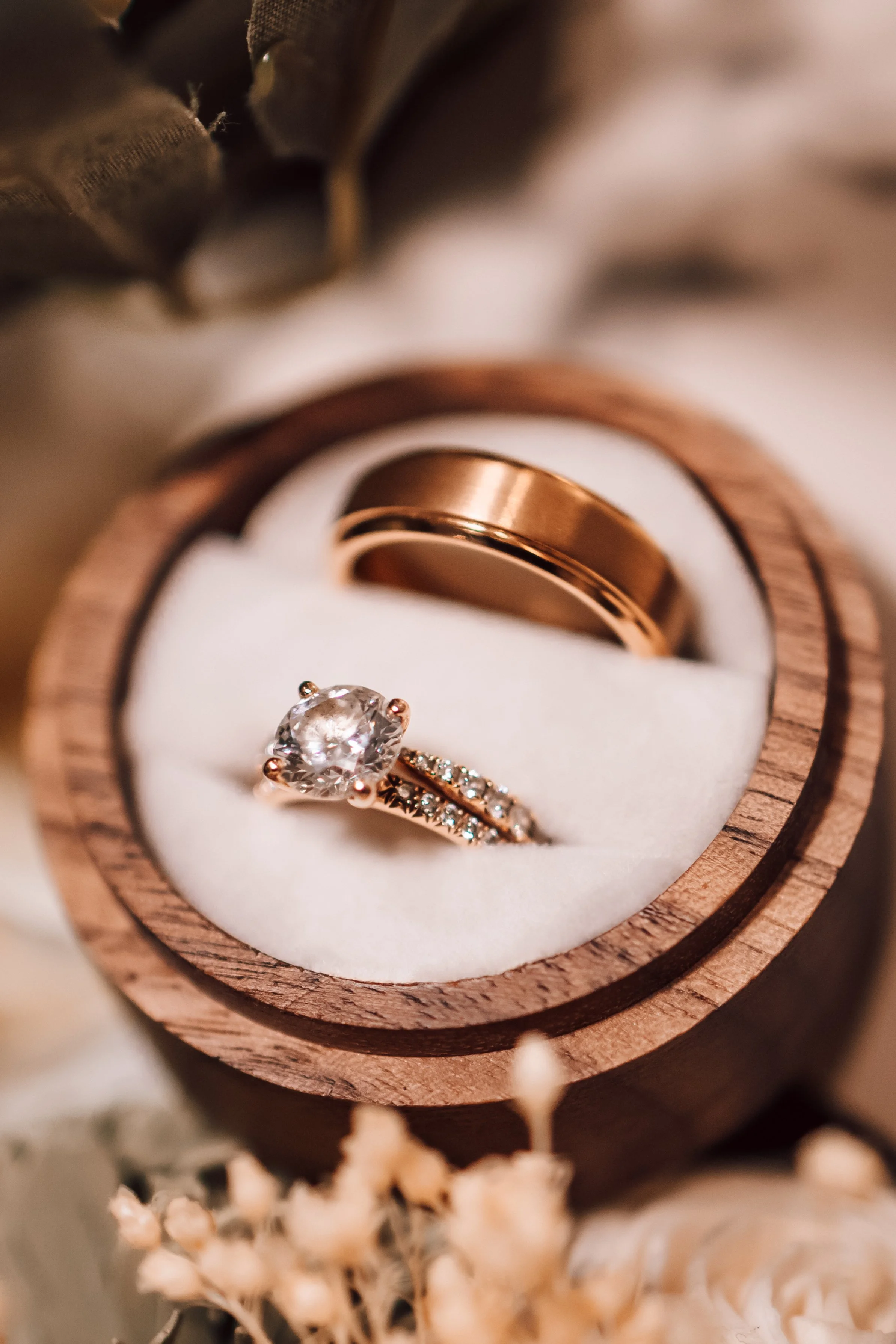 Close-up of a wooden ring box containing a diamond engagement ring with a large center stone and smaller stones on the band, and a plain gold wedding band.
