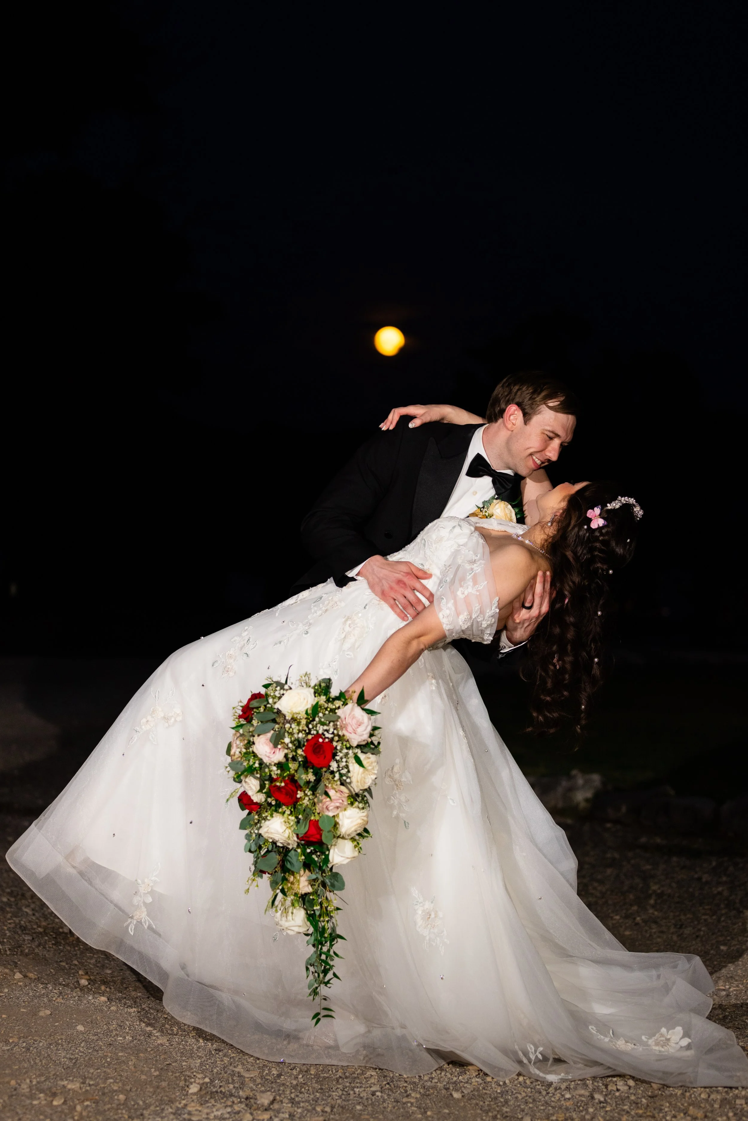 A bride and groom sharing a romantic dance outdoors at night, with the moon in the background.