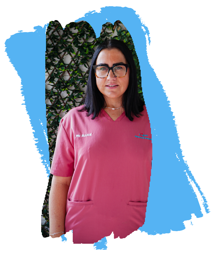 A woman with black hair wearing glasses and a pink scrub top standing in front of a leafy background.