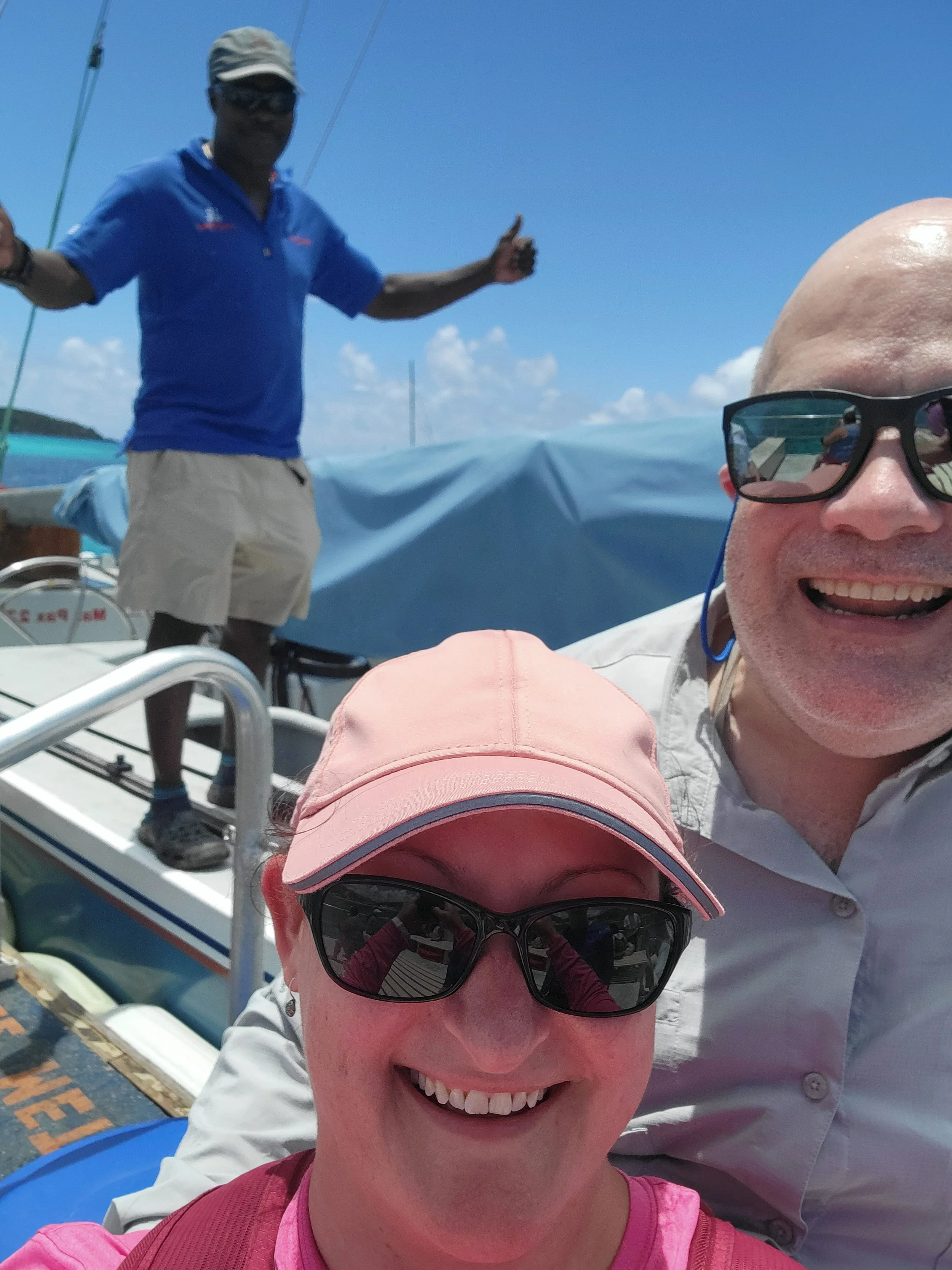 Couple in the sun with man in background giving thumbs up