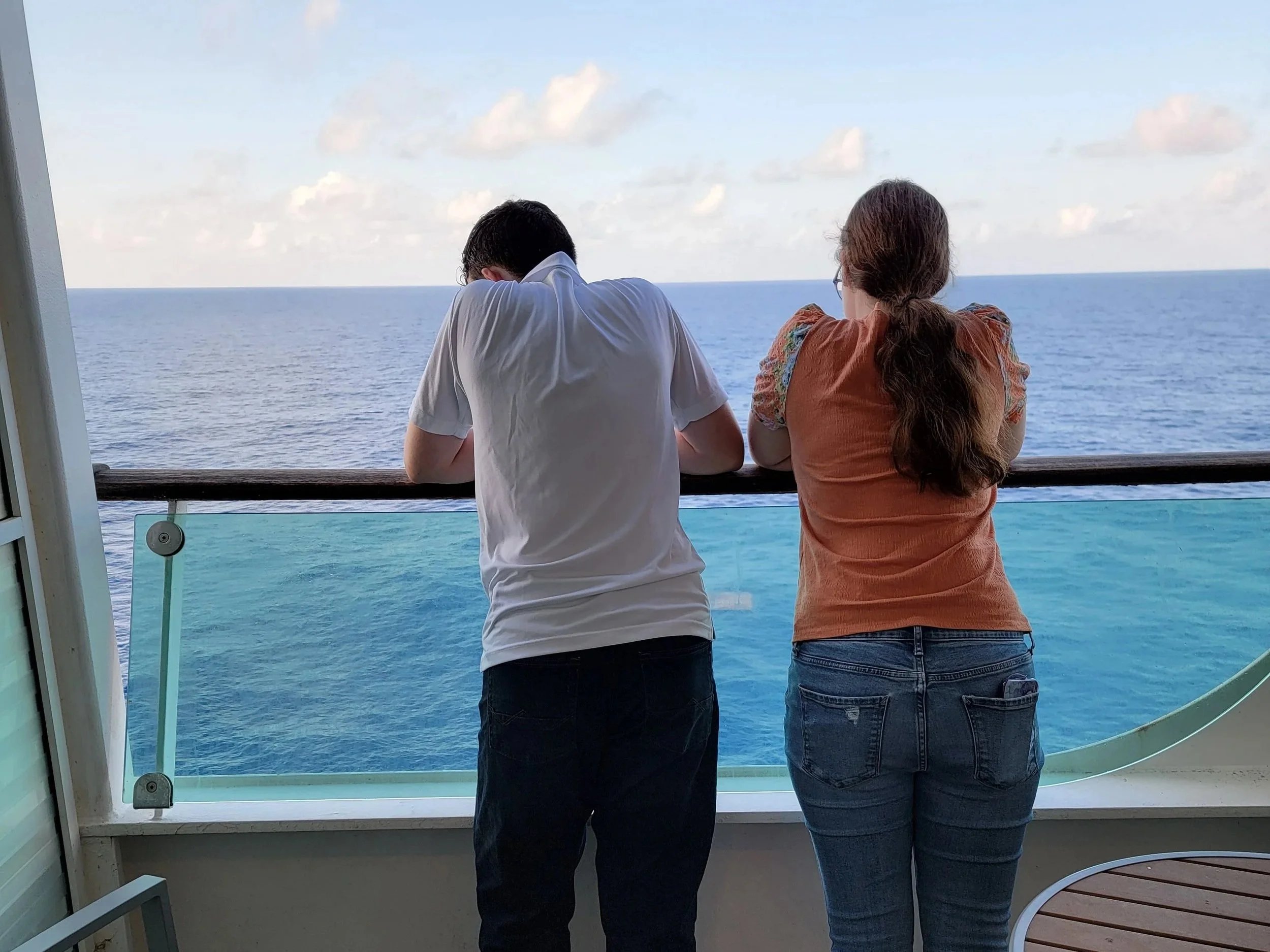 young man and woman facing ocean on cruise ship balcony