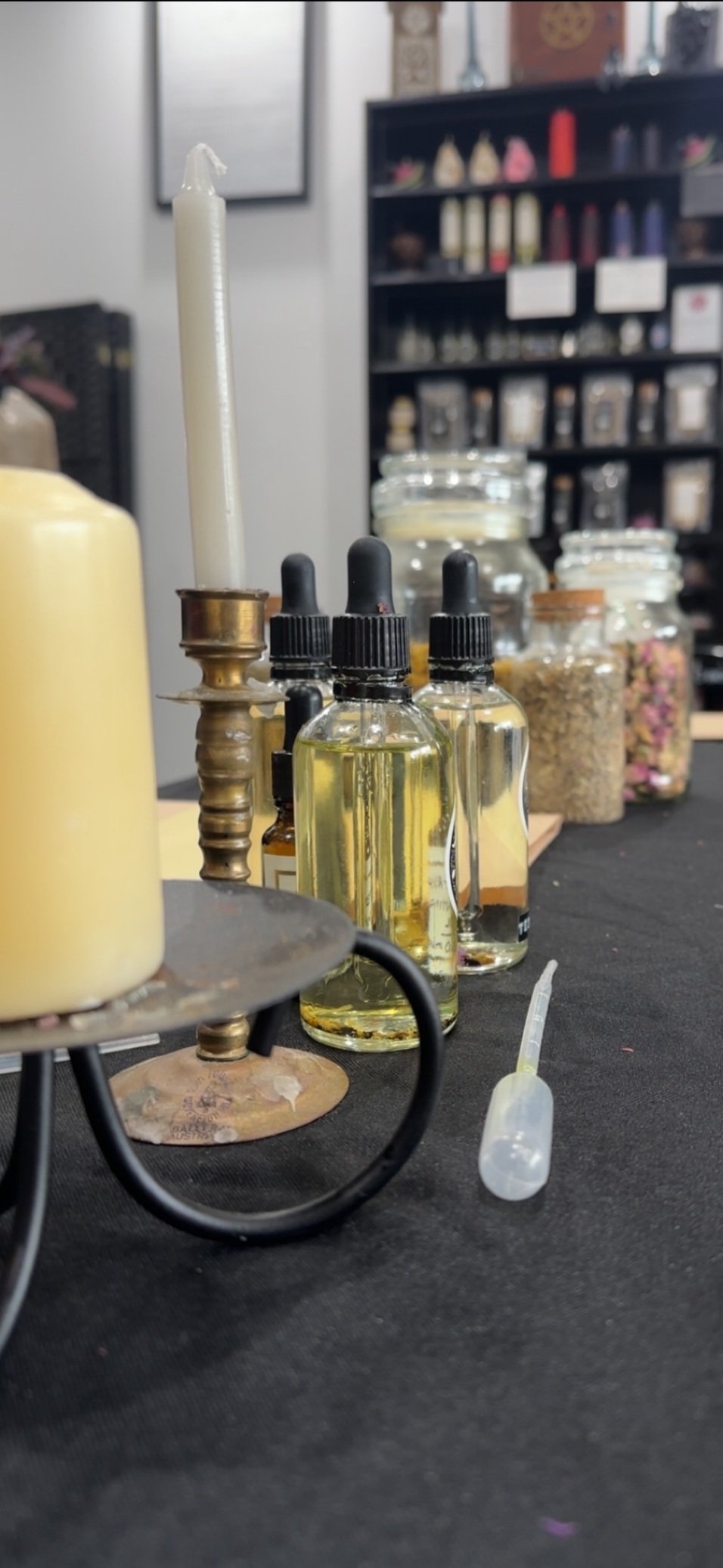 Essence bottles, a candle, and small jars of herbs or ingredients on a black table, likely in a herbal or aromatherapy setting.