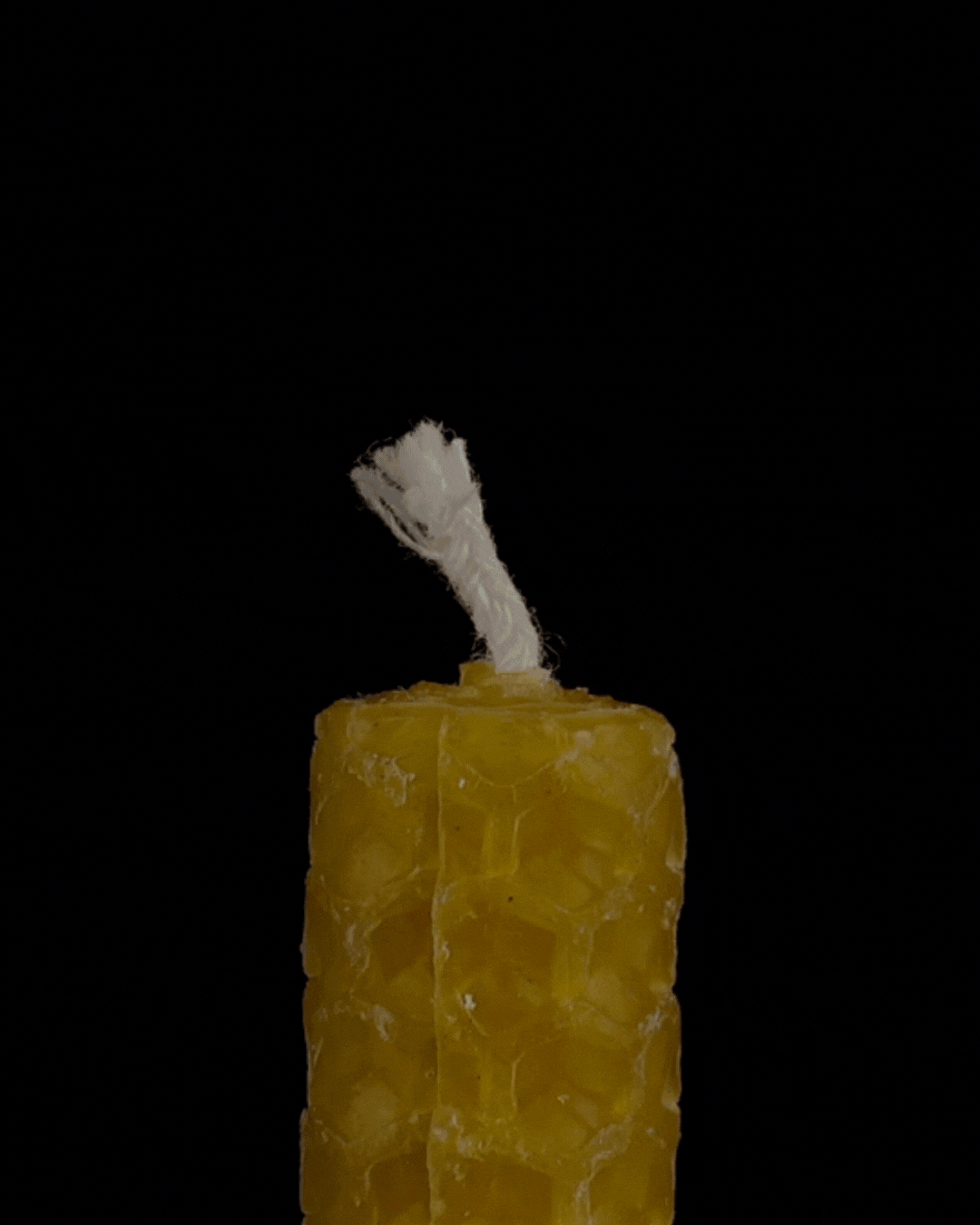 A yellow beeswax candle with a white wick against a black background.