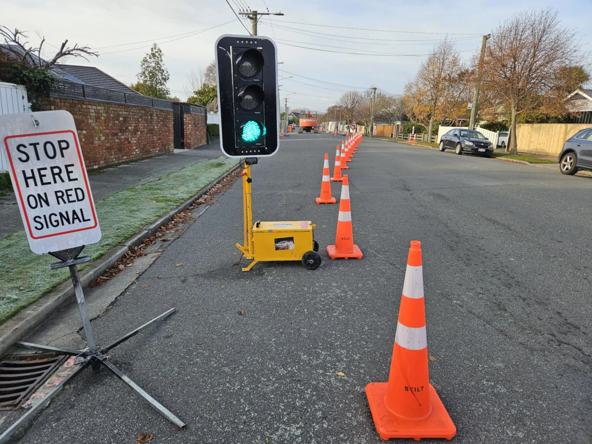 A green traffic light is on, with orange traffic cones lining the street. A sign instructs to stop here on red signal, alongside a construction zone or road work area.