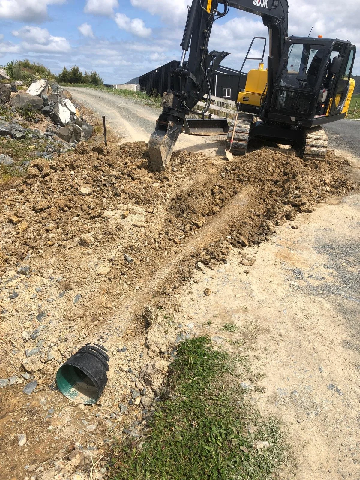 Excavator on dirt road with exposed drainage pipe