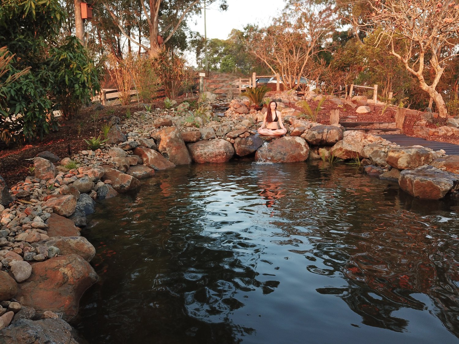Panoramic view of a woman sitting on the edge of a flo garden natural swimming, sitting in meditation position