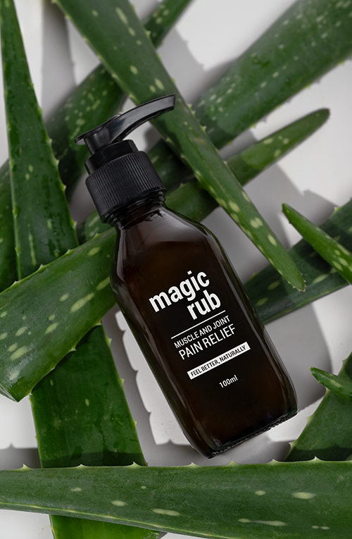 A brown spray bottle labeled 'magic rub' surrounded by aloe vera and cactus plants.