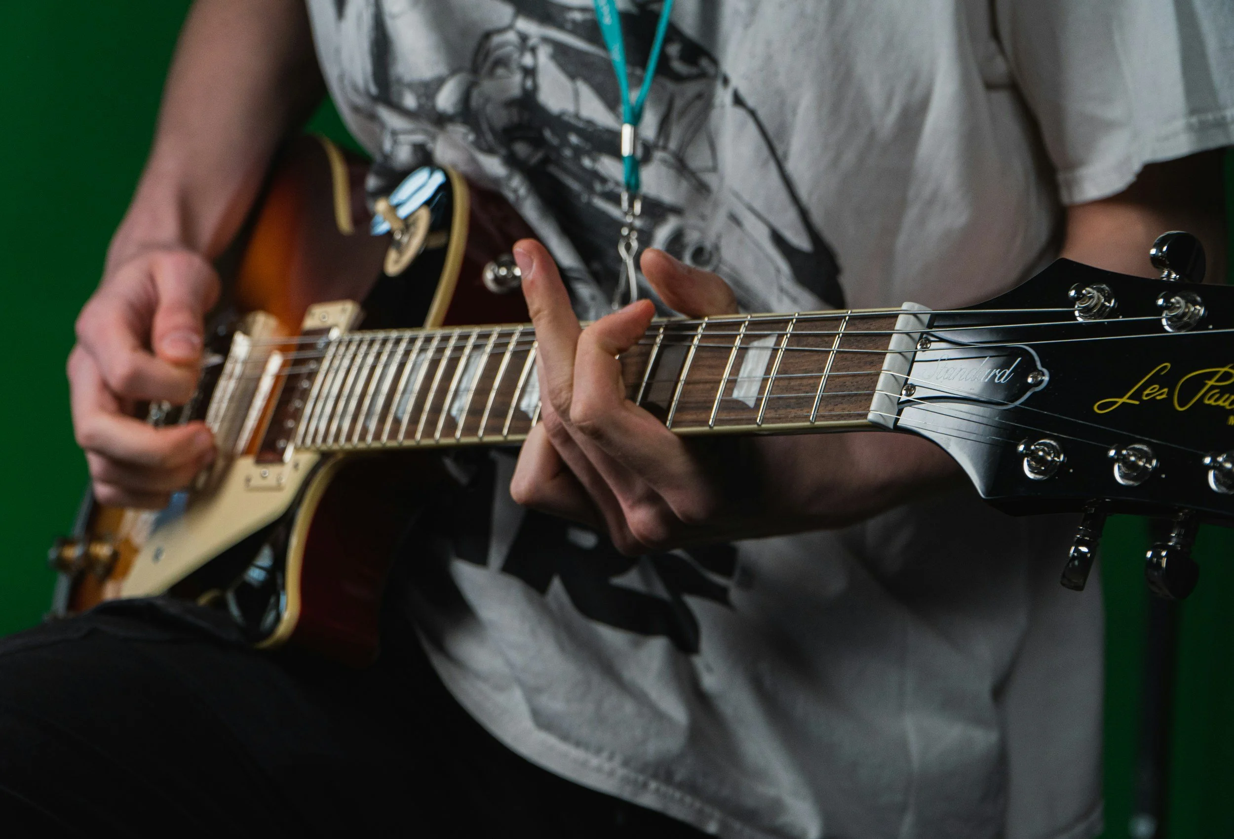 Person playing an electric guitar, focusing on their hands and the guitar neck, with a green background.
