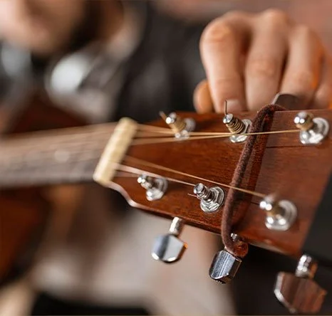 Close-up of a person's hand adjusting tuning pegs on an acoustic guitar's headstock.