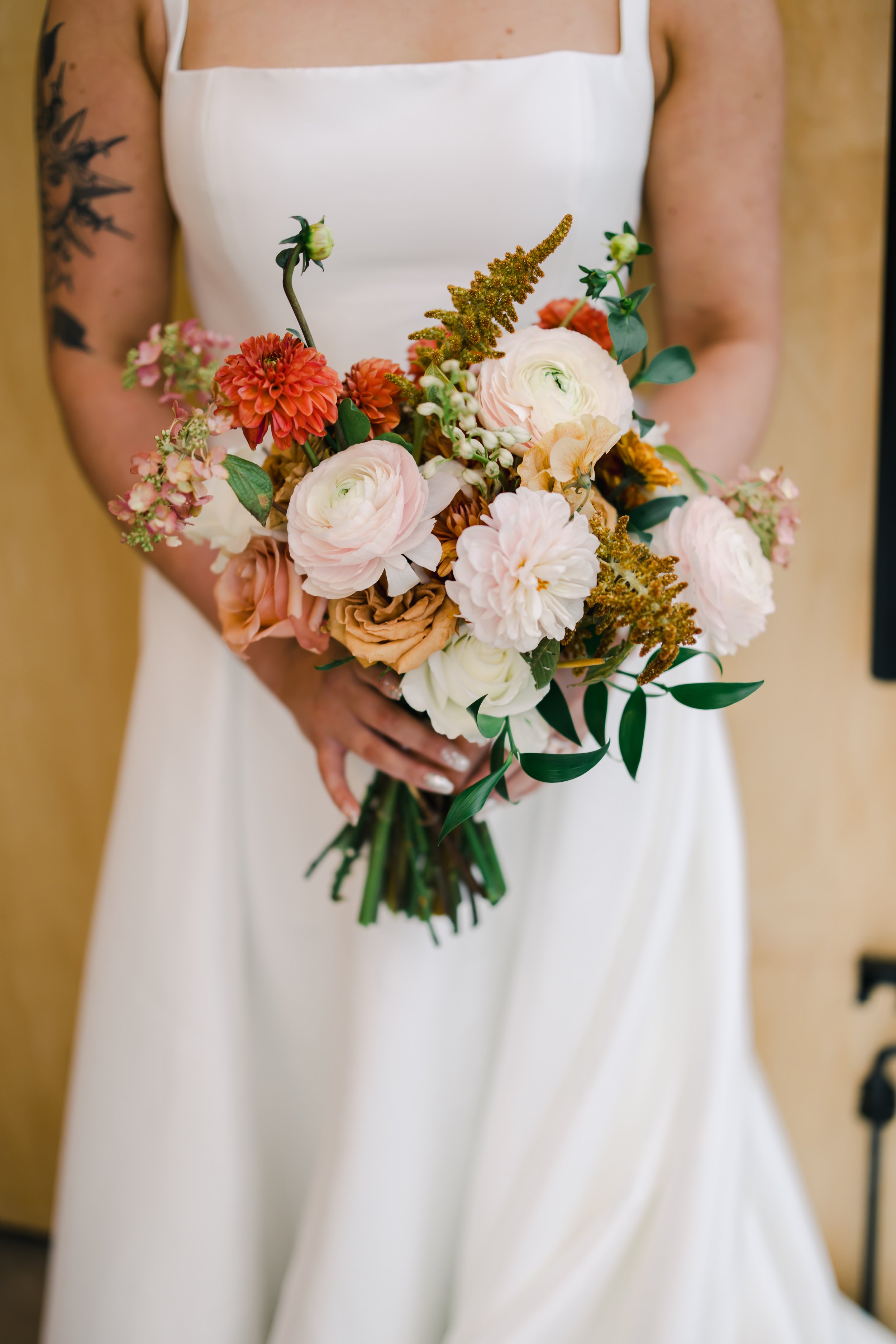 A bride in a white dress holding a bouquet of pink, peach, white flowers and greenery.