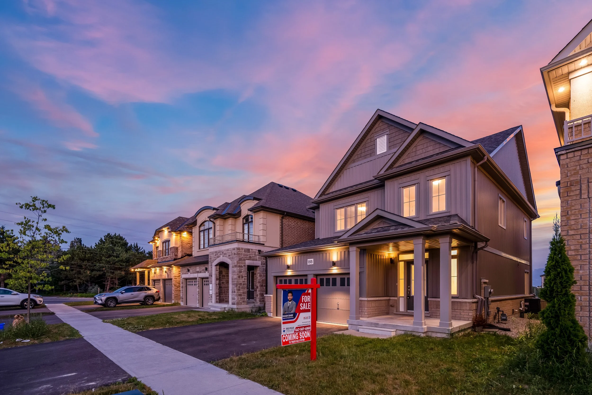 Row of modern houses at sunset, with a for sale sign in the front yard of the house on the right.