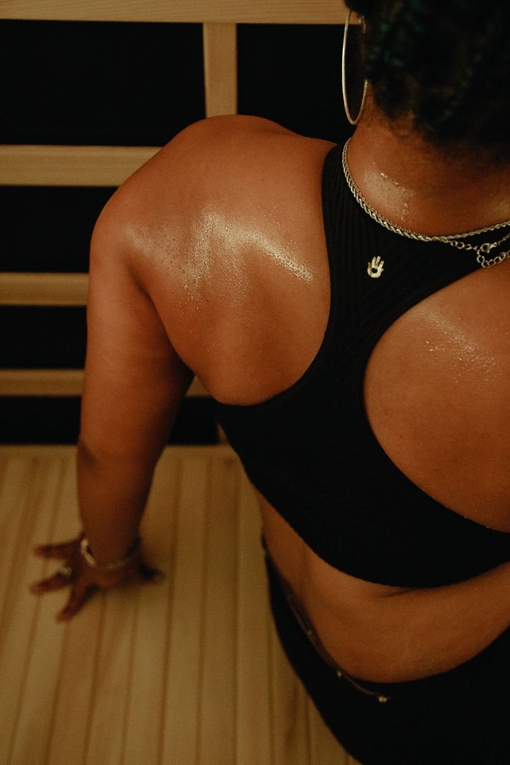 A woman meditates in an infrared sauna wearing a black sports bra and silver necklace