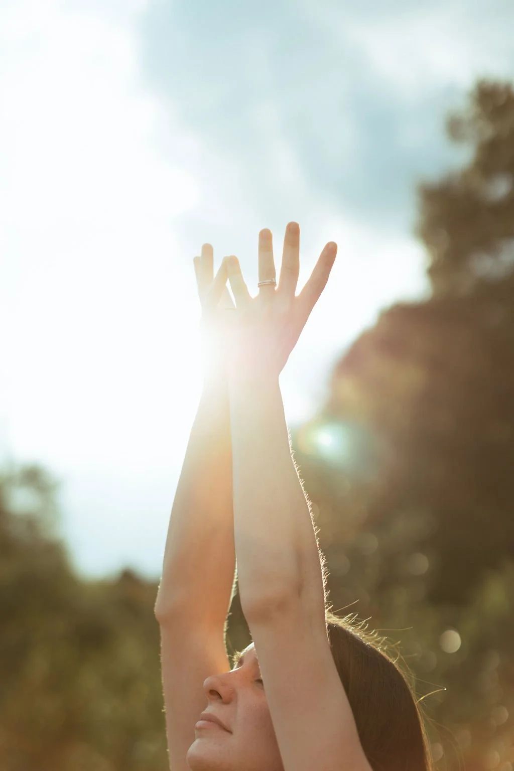 Person with raised arms and a lotus mudra in sunlight, blurred background