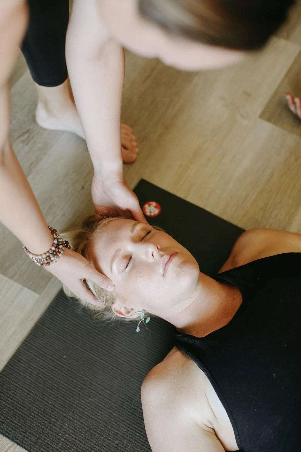 Woman receives a head massage and neck therapy during her prenatal yoga class while lying down on her yoga mat.