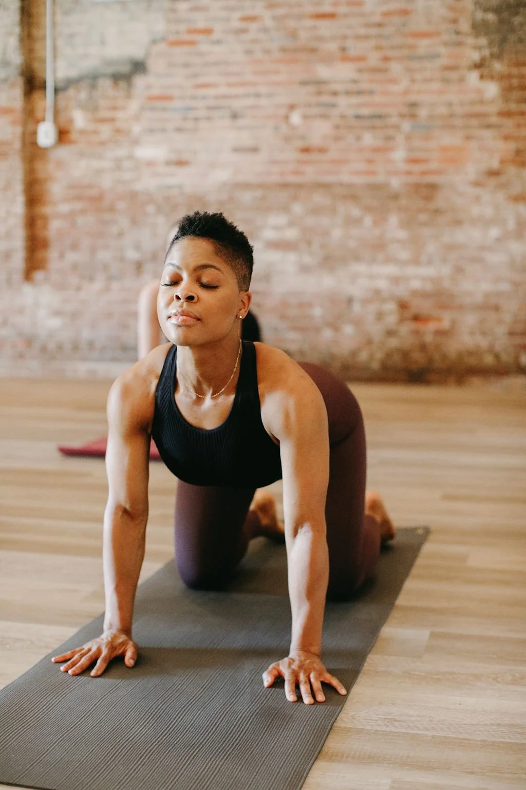 A woman performs tabletop pose in a group yoga class in a studio with brick walls and hardwood floors