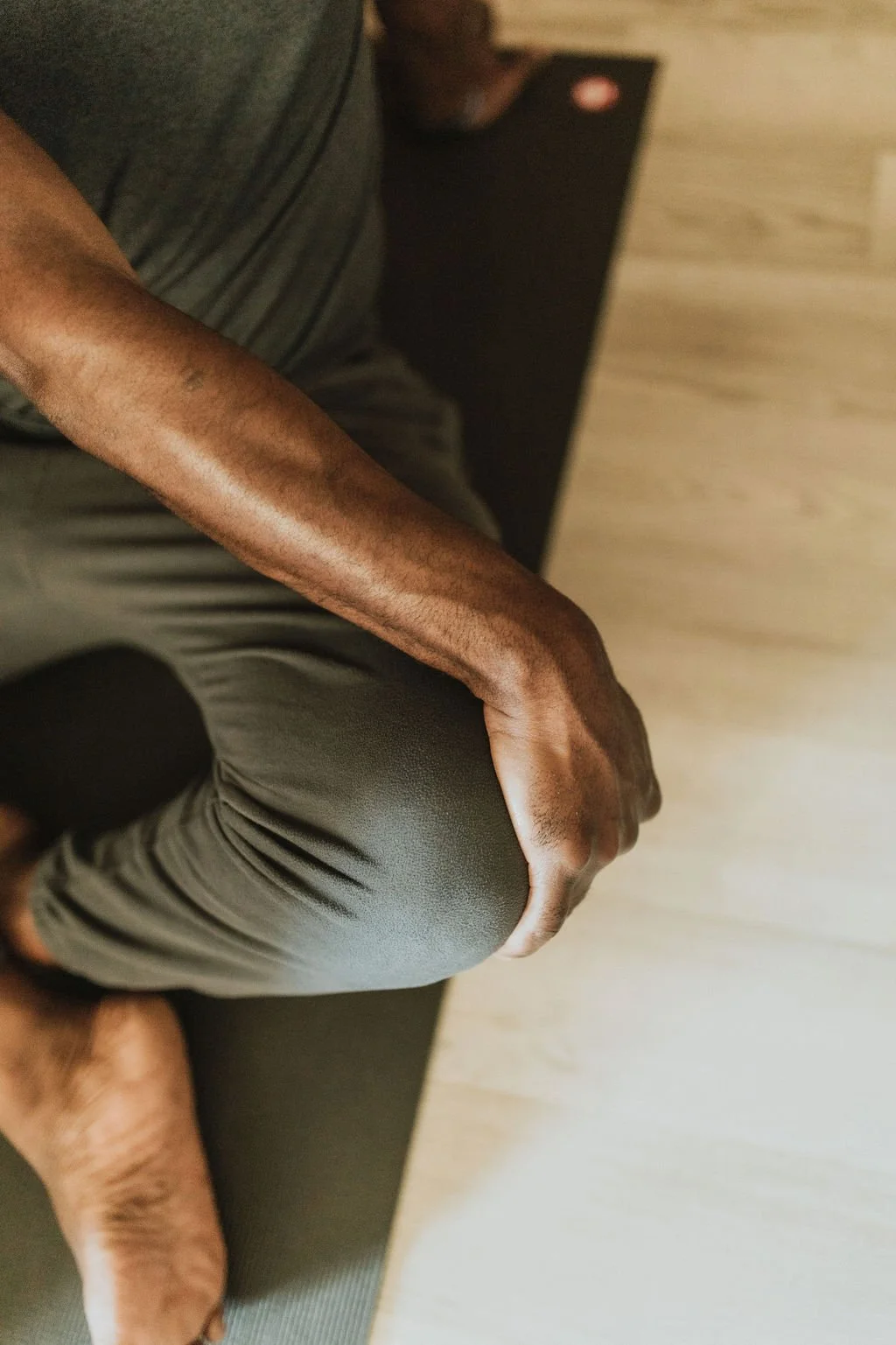 A man is seated on a yoga mat with his hand holding his opposing knee
