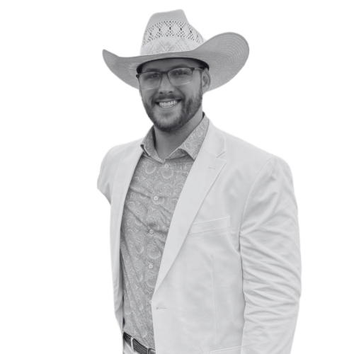 Man wearing a cowboy hat, glasses, a light-colored blazer, and a patterned shirt, smiling at the camera.