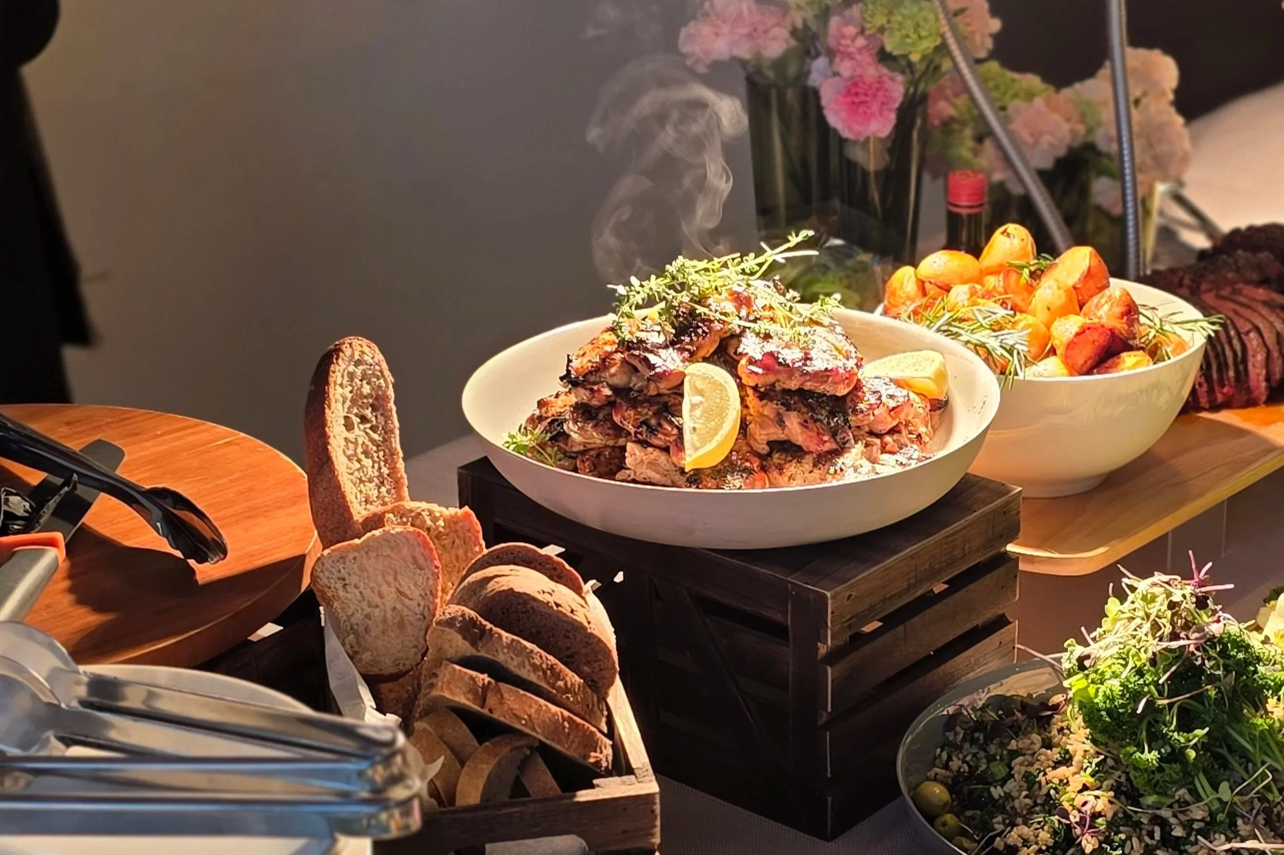 A food display as part of a loaded carving station with all the trimmings. Featuring specialty meats, garnished with lemon slices,  roasted potatoes, a variety of breads, endless salads and other dishes not pictured.