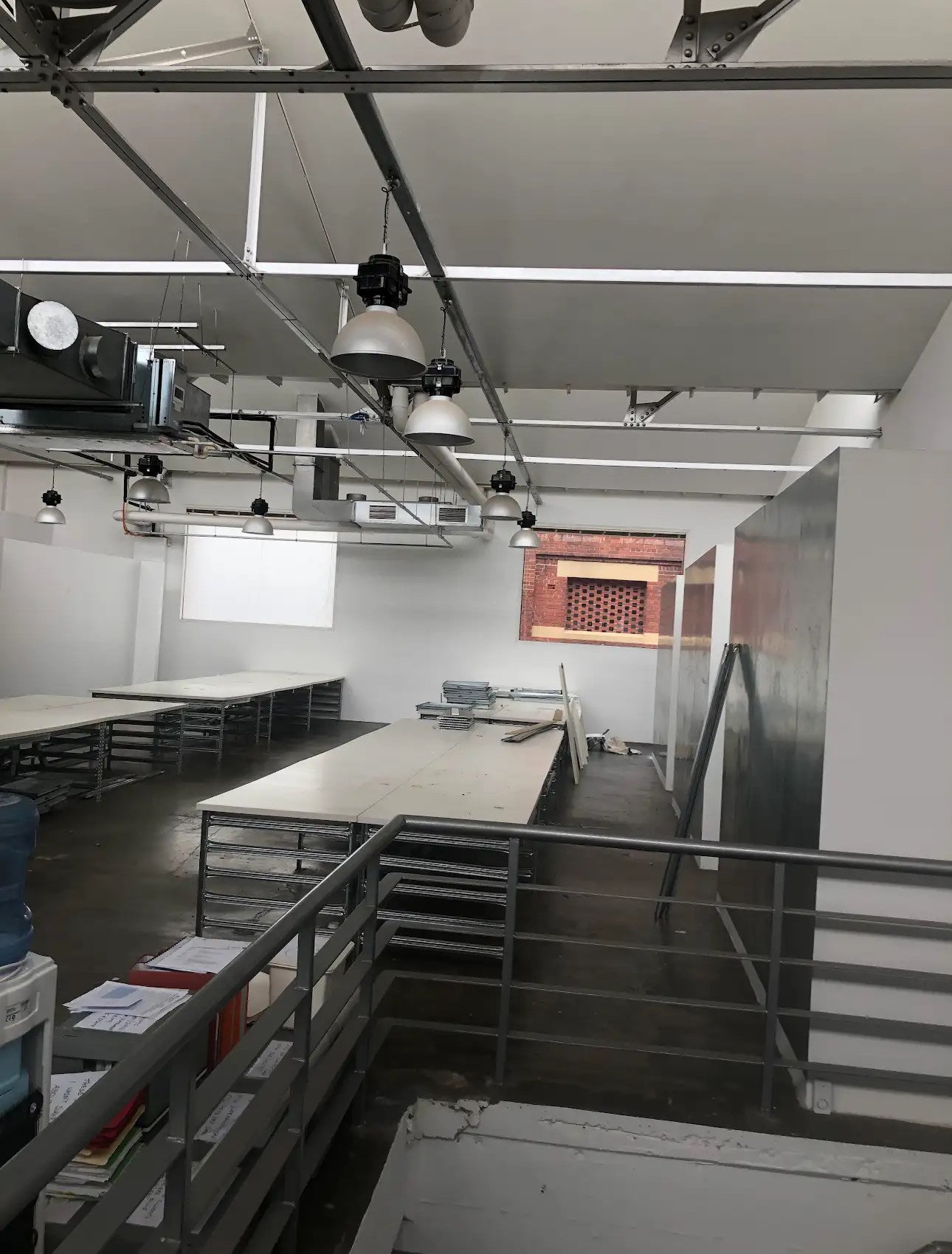 Interior of an industrial-style room with metal beams, hanging lights, long tables, and a window.
