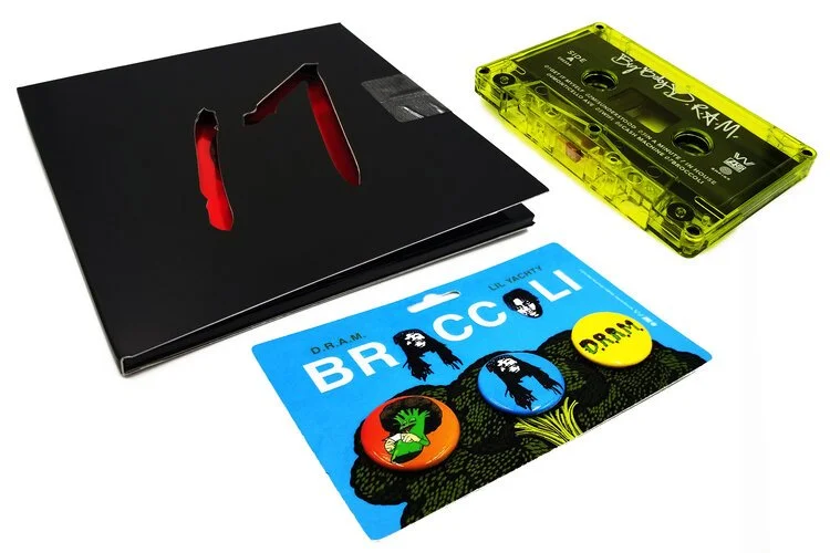 Black vinyl record cover with red design, neon green cassette tape labeled "D.R.A.M.", and a card with colorful buttons featuring broccoli graphics.