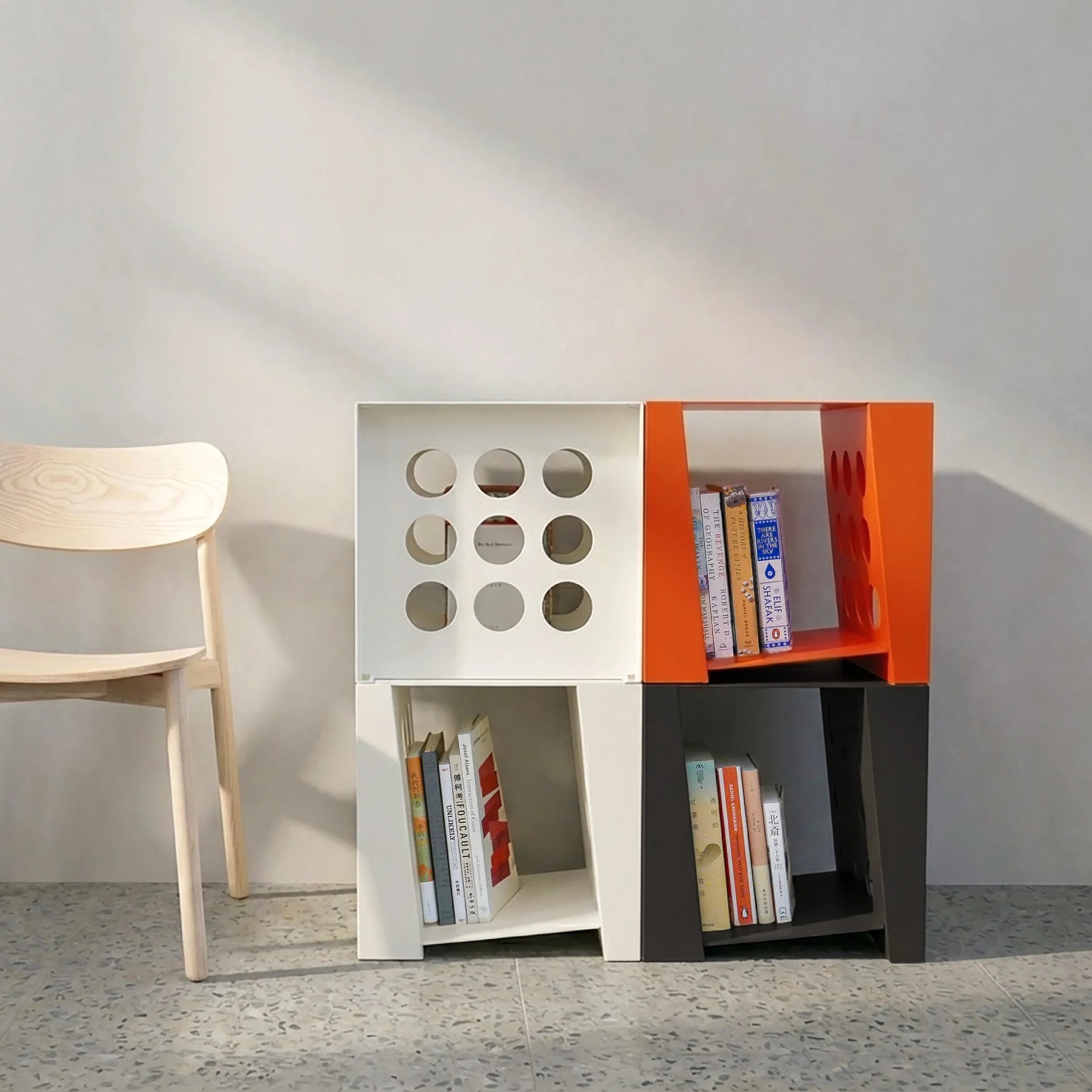 Colorful modern bookshelf with books, next to a light wooden chair against a plain wall.