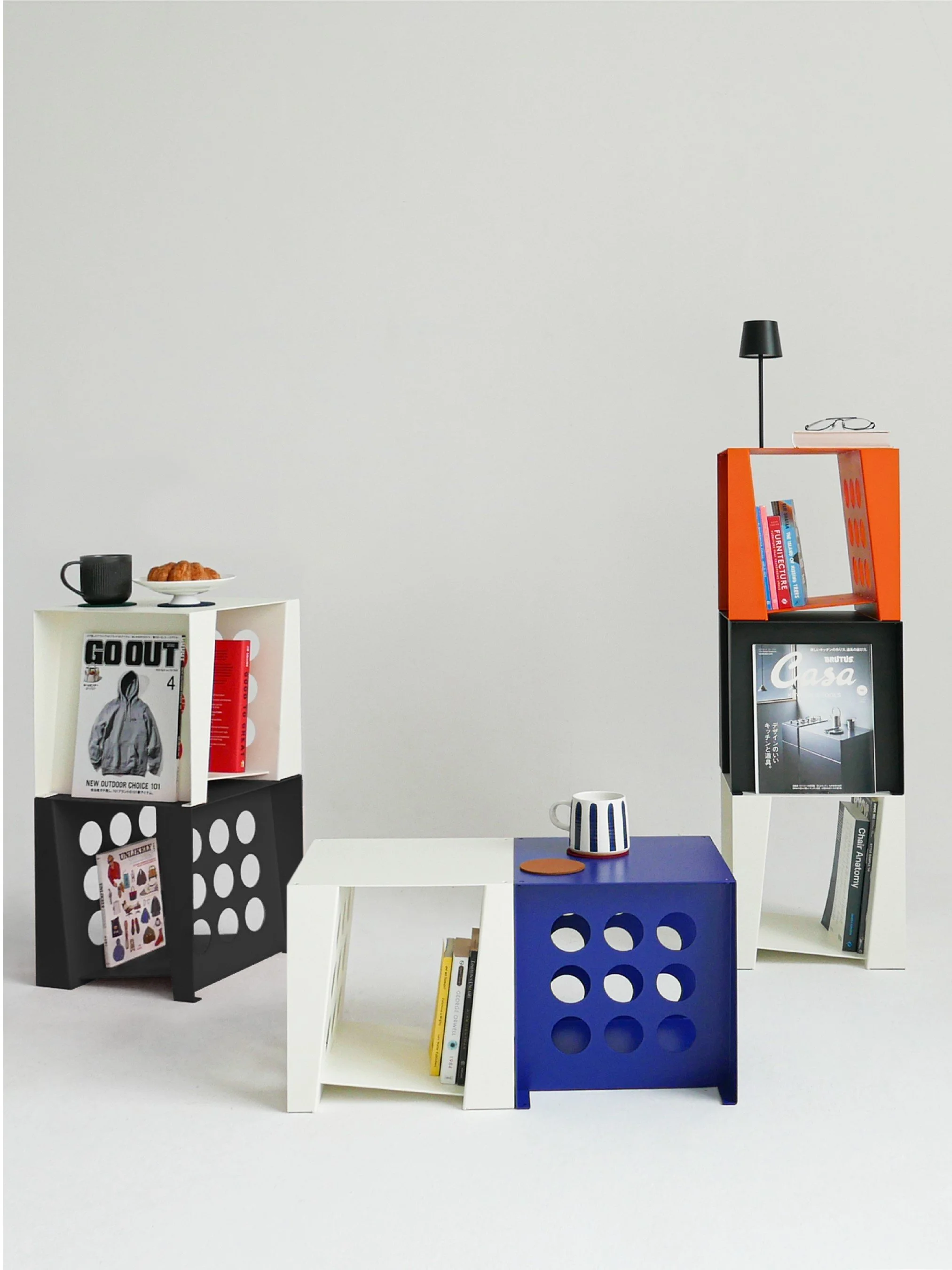 Colorful geometric bookshelves with books, a mug, a croissant, a small lamp, and glasses in a minimalist setting.