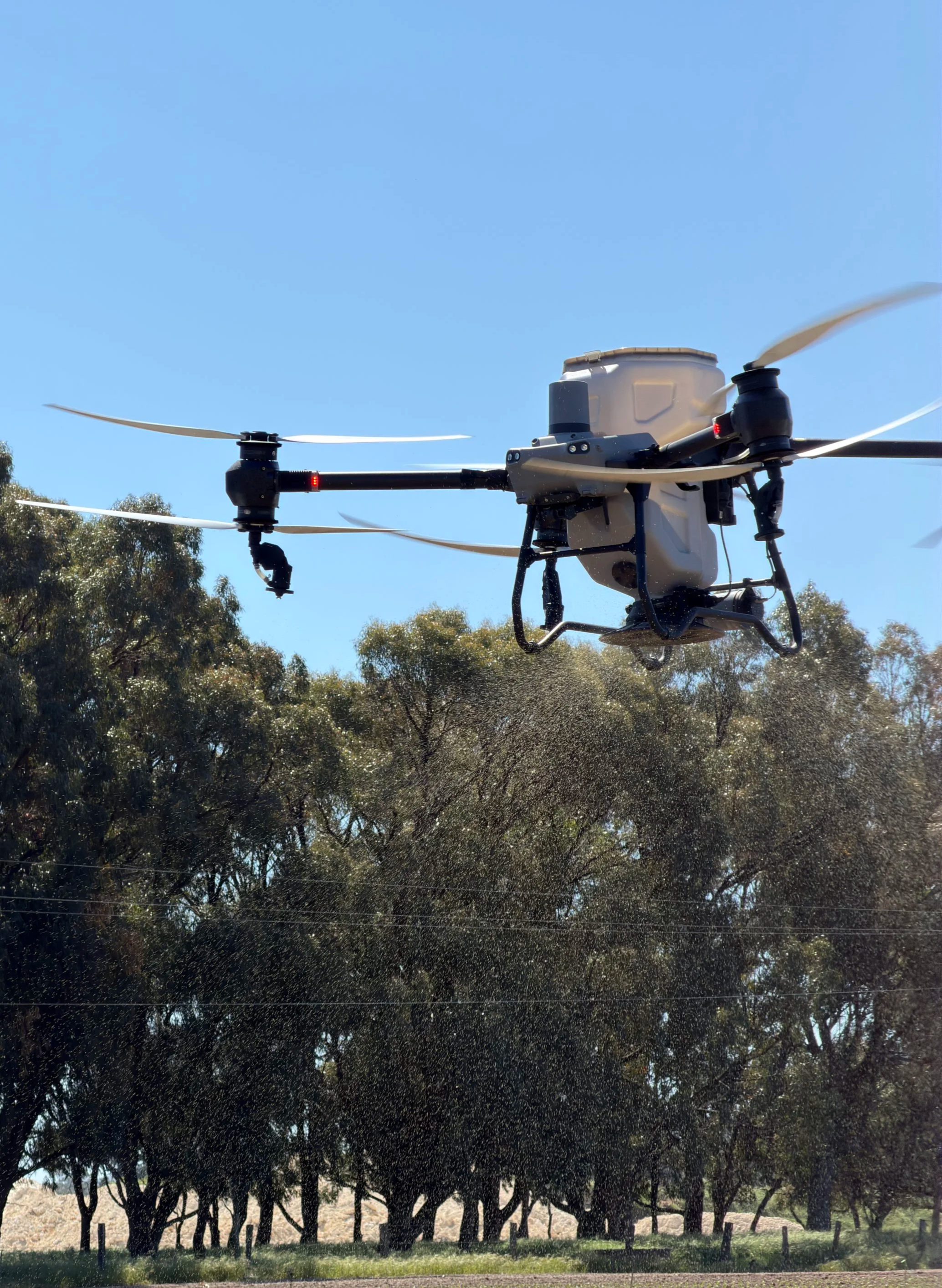 A drone flying outdoors over trees on a clear day.