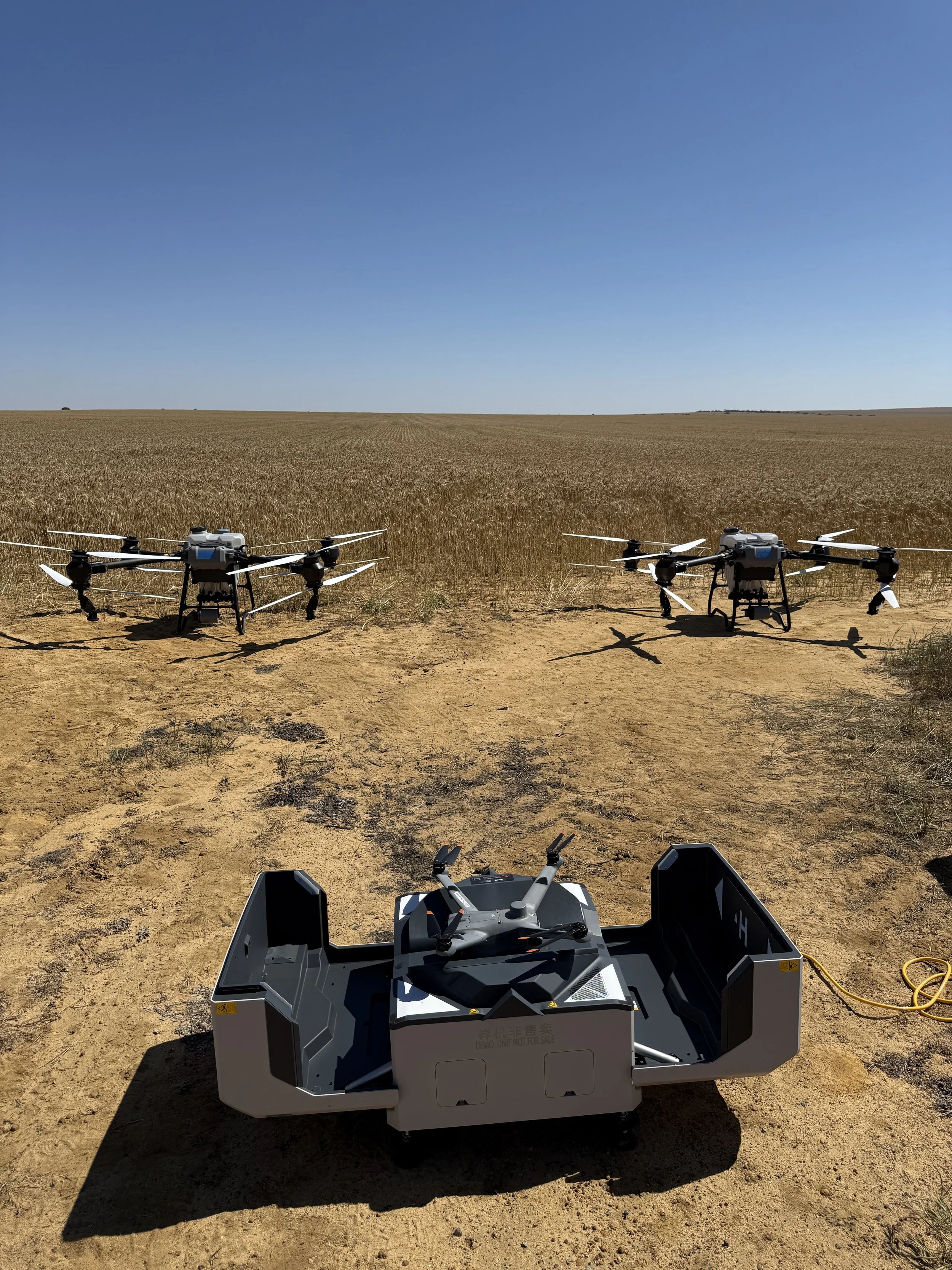 Three drones in a field with dry soil and a wide open sky.