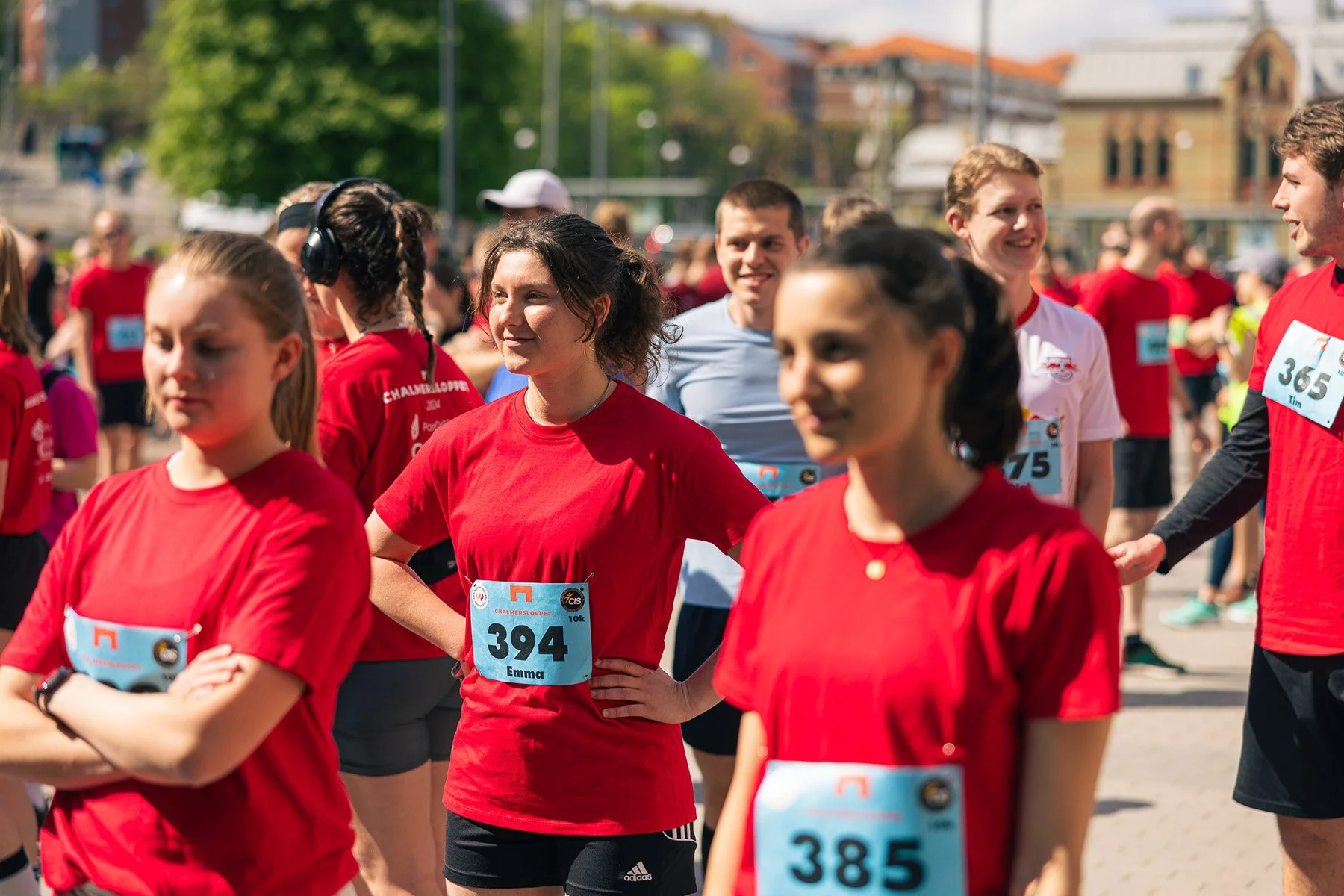 Grupp människor som deltar i ett fysiskt löpevent utomhus, många bär röda T-shirts och har medaljer runt halsen, med nummerlappar på bröstet.