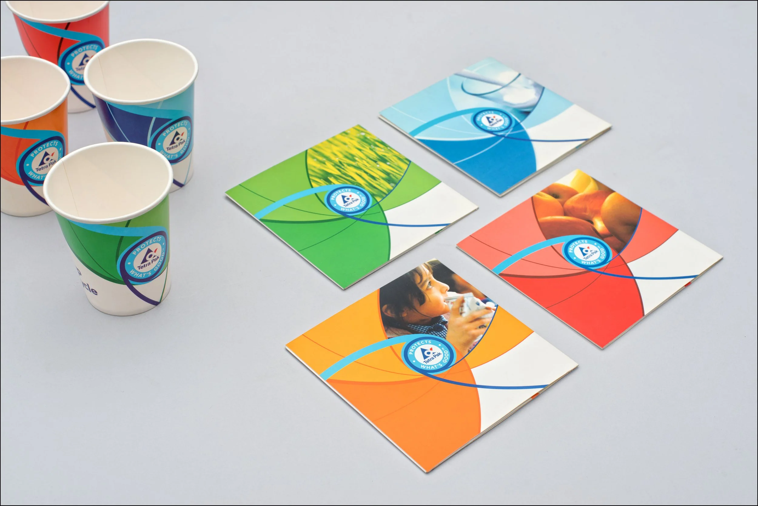 Colorful paper cups and informational brochures with a logo featuring a soccer ball, circle, and slogan, arranged on a light gray surface.