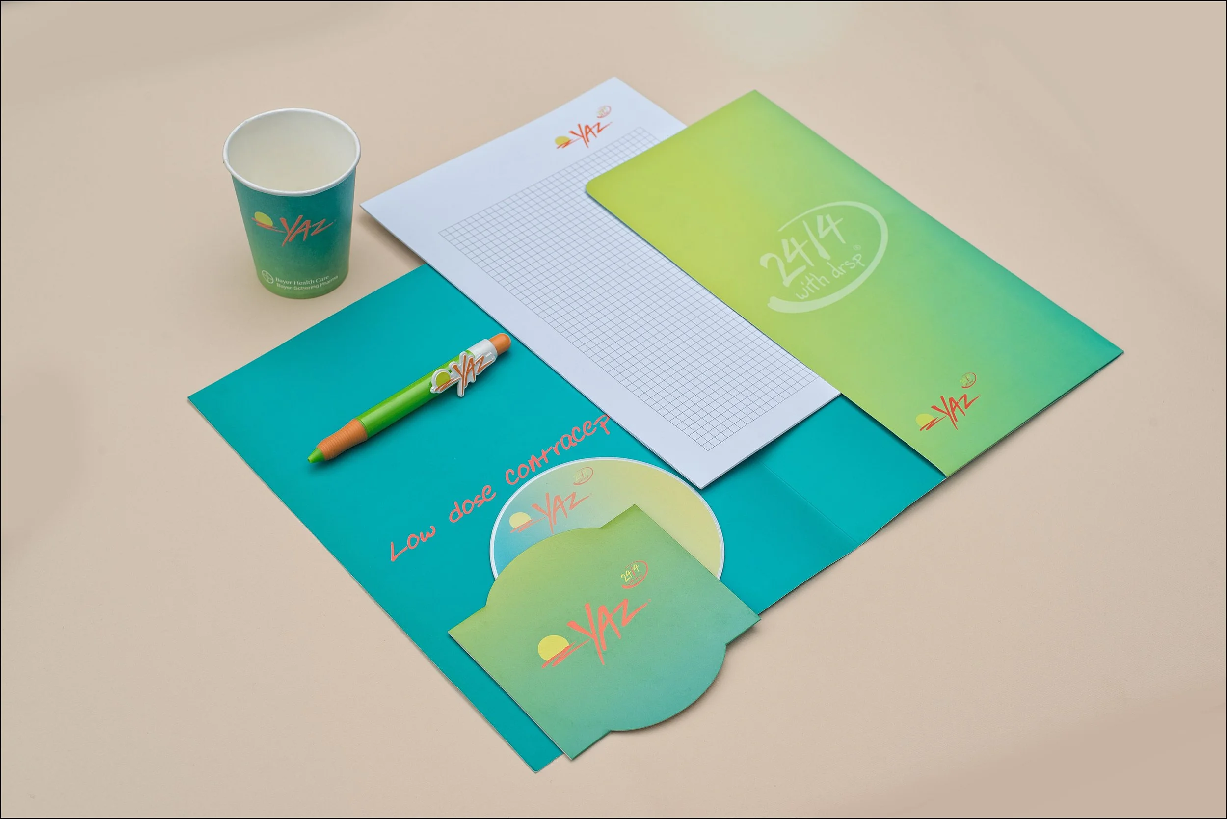 Desk with colorful printed materials, a cup, and a pen, all branded with the Yaz logo.