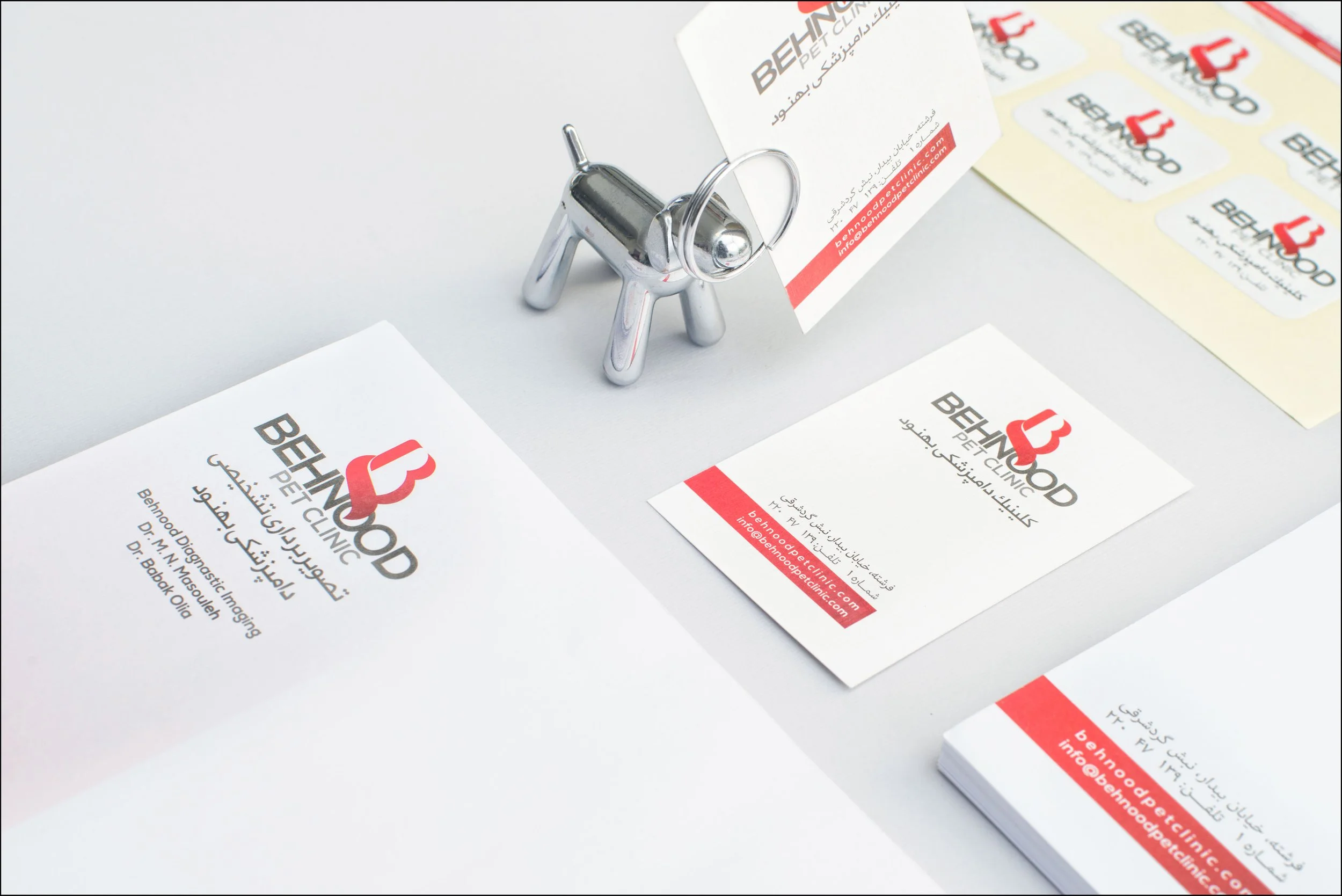 Business cards and stationery for Behnood Pet Clinic, featuring a chrome dog figurine holding a business card, with additional business cards and stickers on a white surface.