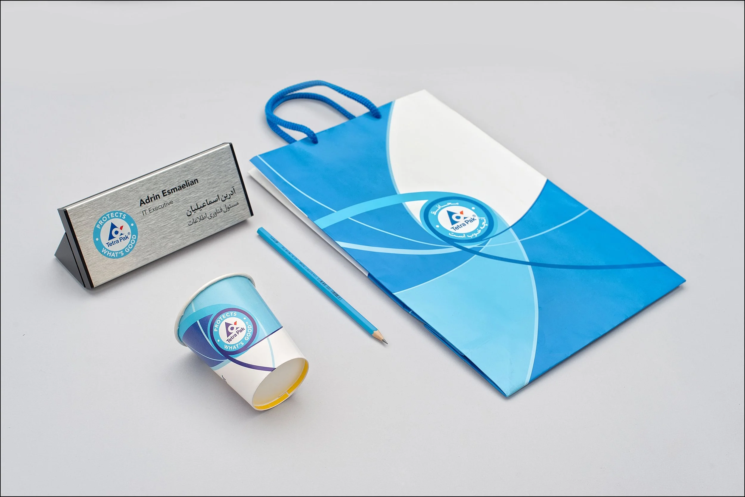 Business conference items including a nameplate, paper cup, pen, and tote bag, all branded with Tetra Pak logo and blue color scheme.