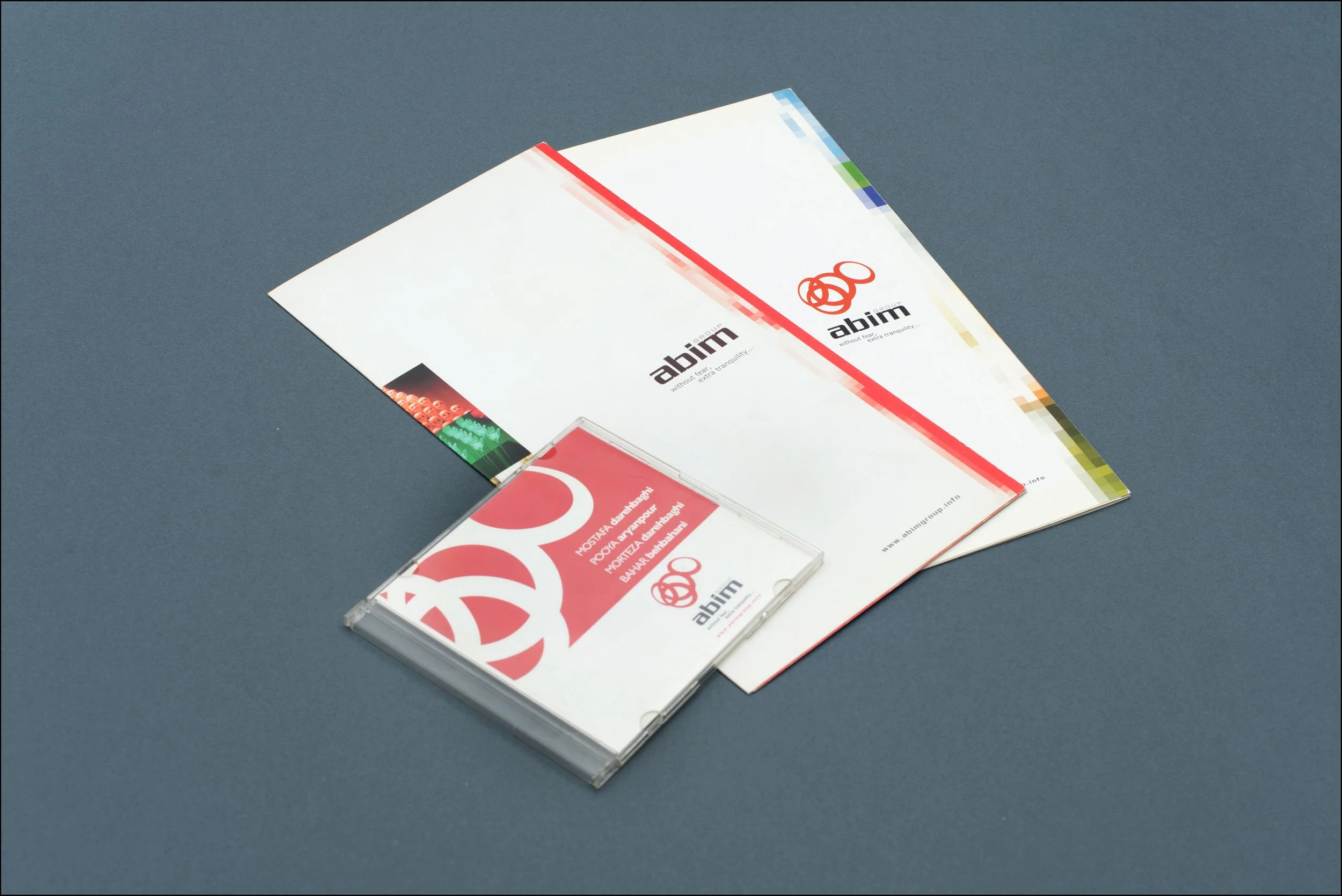 Branded stationery and a business card on a gray surface. The stationery has logos with red and black text and graphics, including the word 'abim'. The business card has red and white colors with the same logo and text.