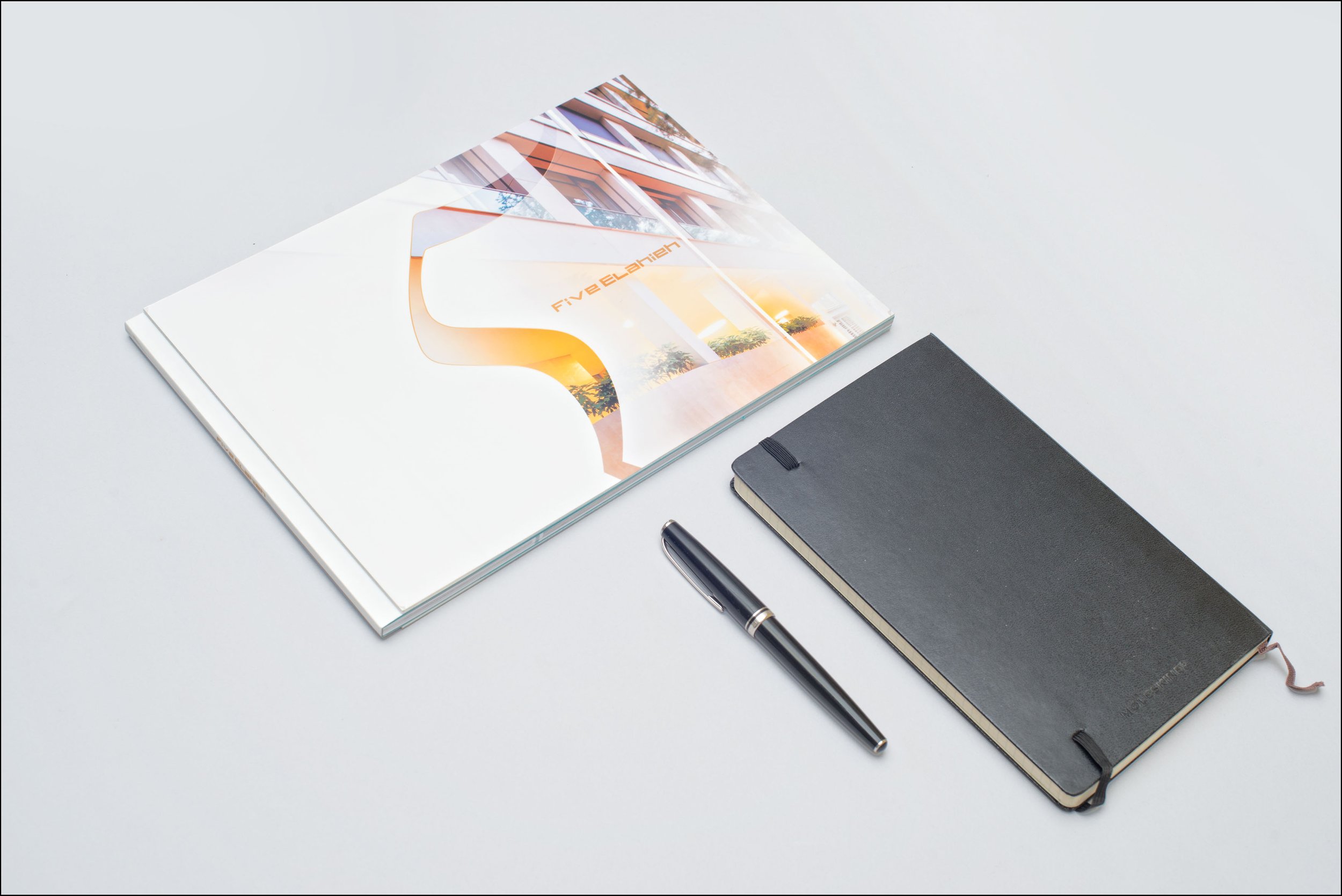 Open magazine, closed black notebook, and black pen arranged on a white desk.