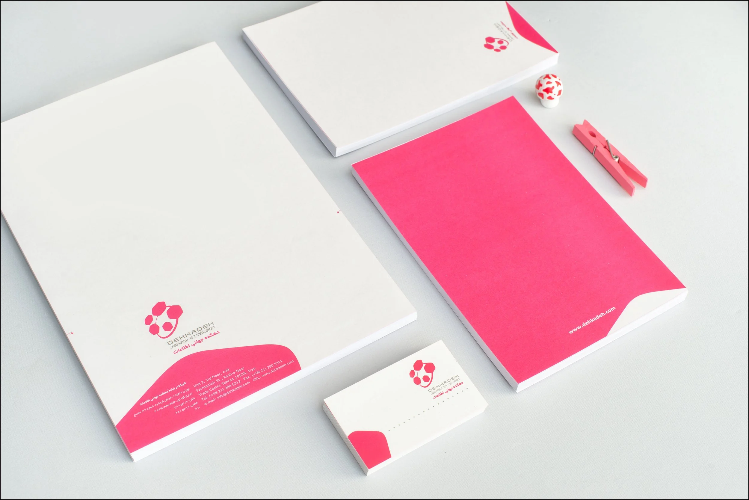 Set of stationery items with a pink and white color scheme, including letterhead, a notepad, a business card, a pink clothespin, and a decorative ball, all with a logo of a hexagonal pattern resembling a rose.