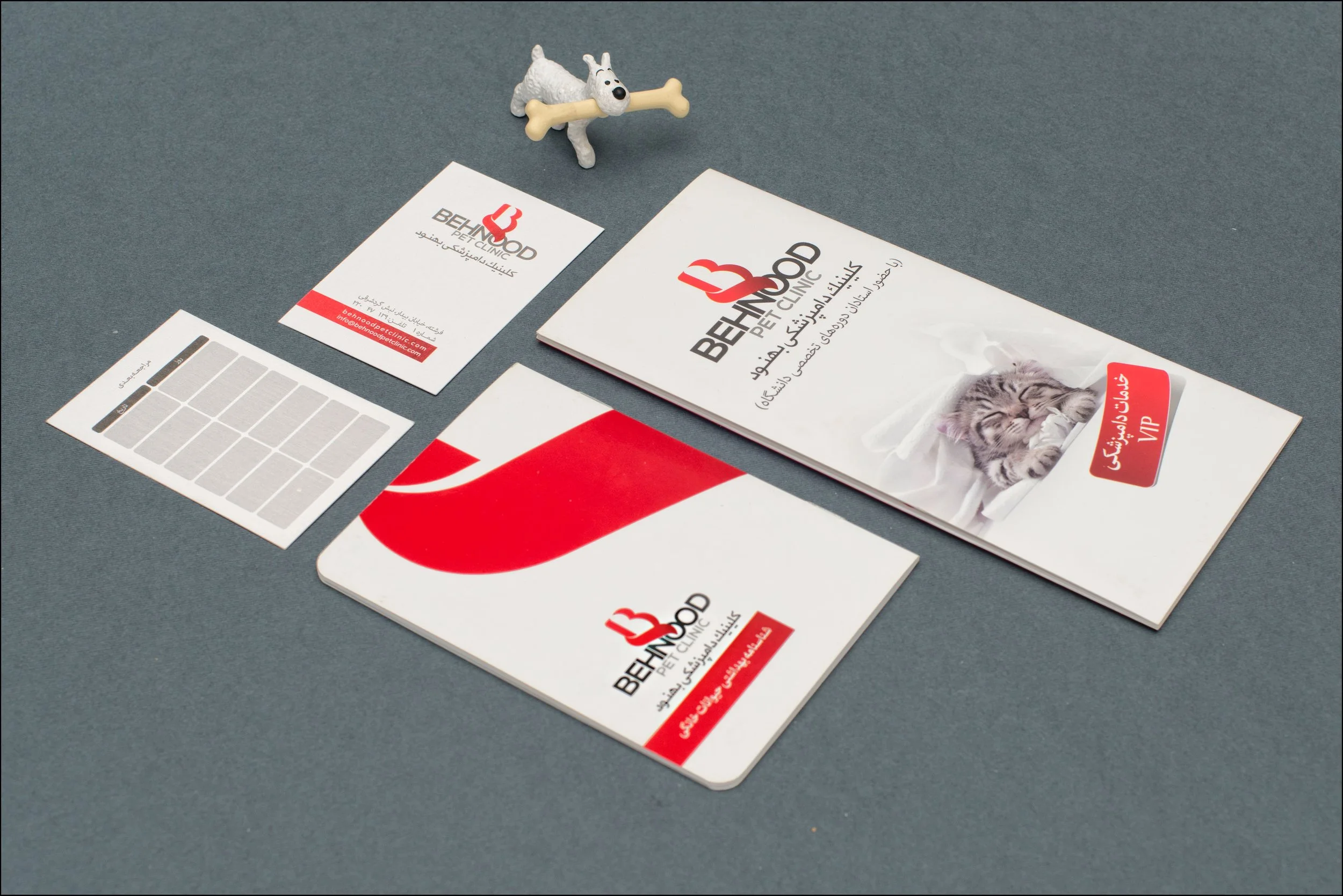 Collection of printed marketing materials for Behnood Pet Clinic, including brochures, cards, and a small toy dog with a bone.