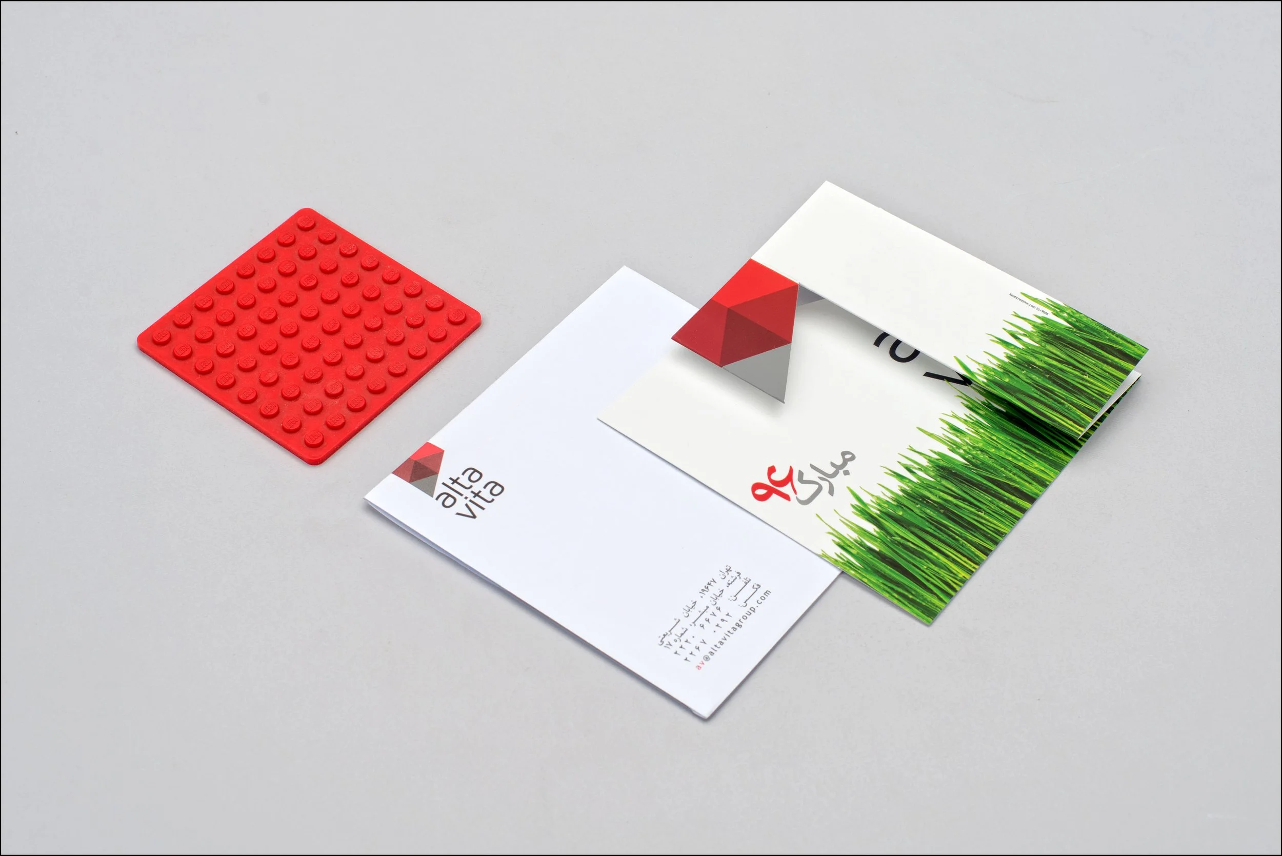 Brochure and business card for Alta Vita, with a red Lego base plate nearby on a light gray surface.