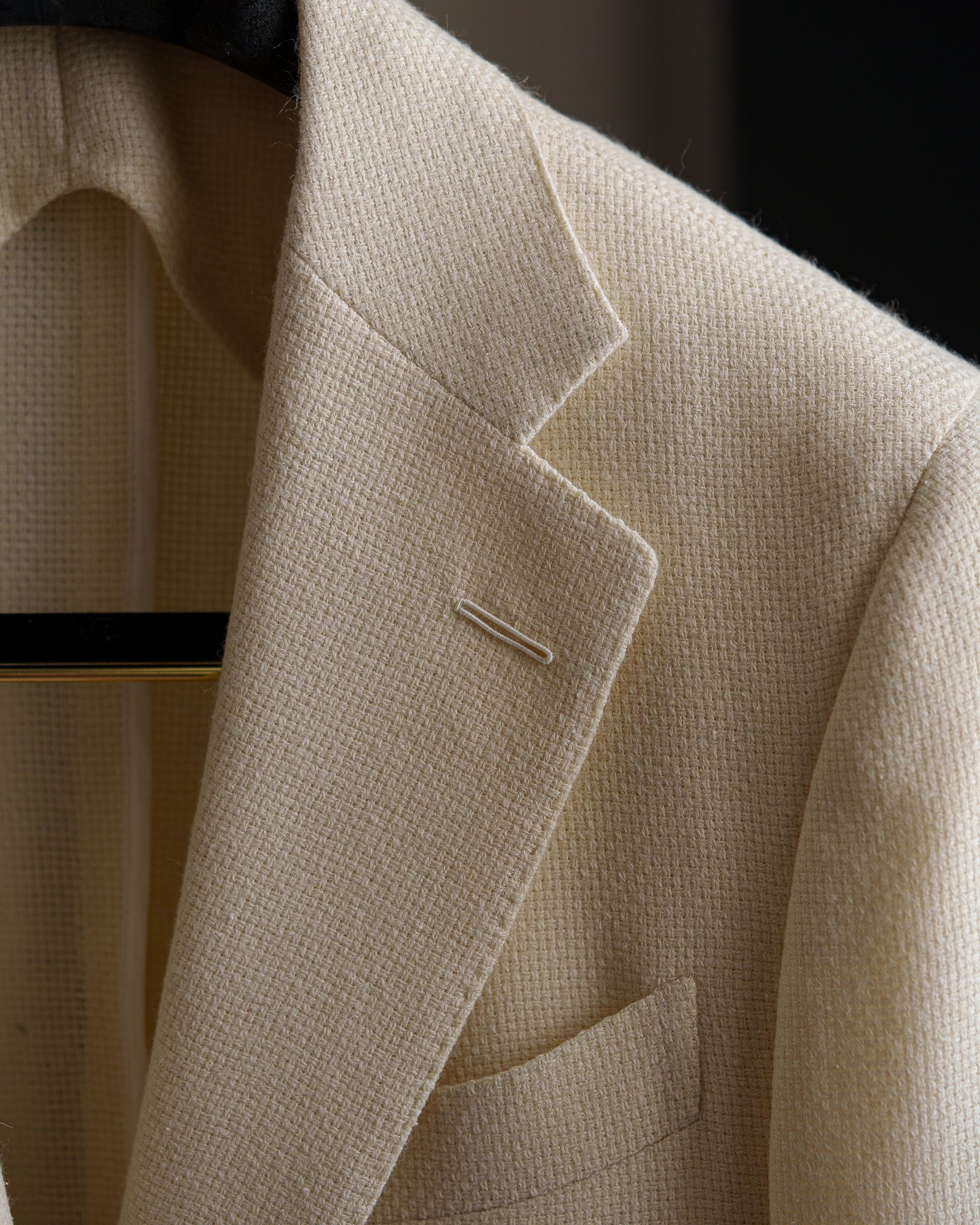 Close-up of a beige textured blazer with a notched lapel and a small pocket on the side.