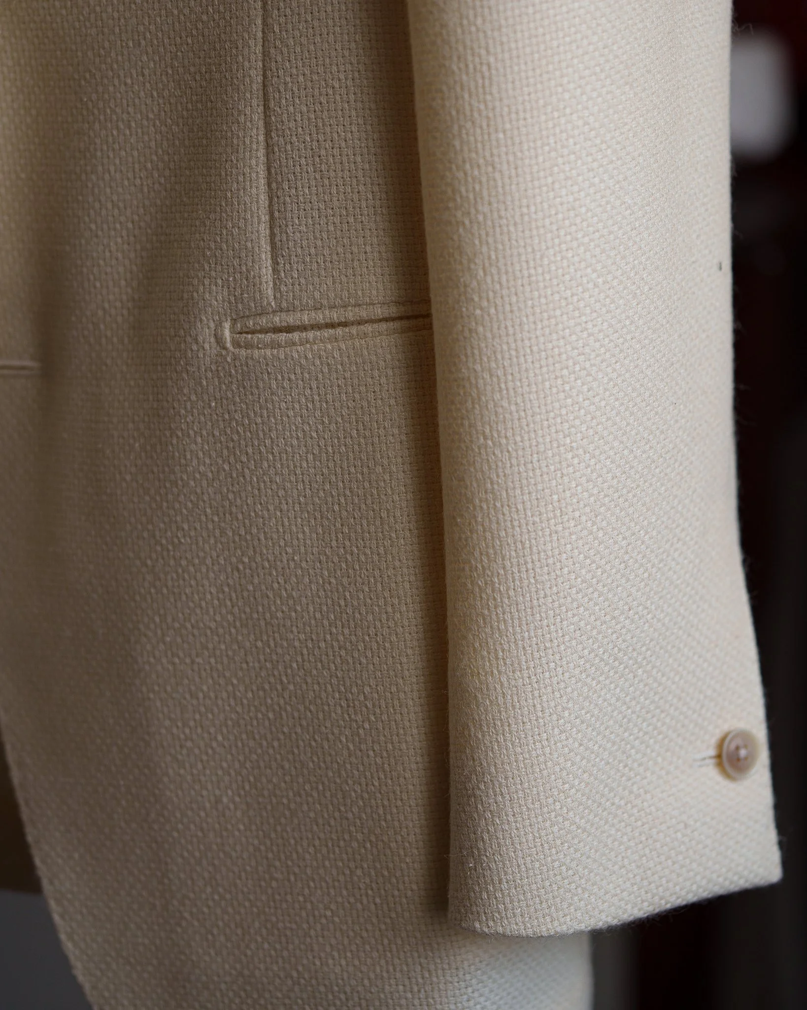 Close-up of a beige textured fabric blazer with a small pocket and button detail.