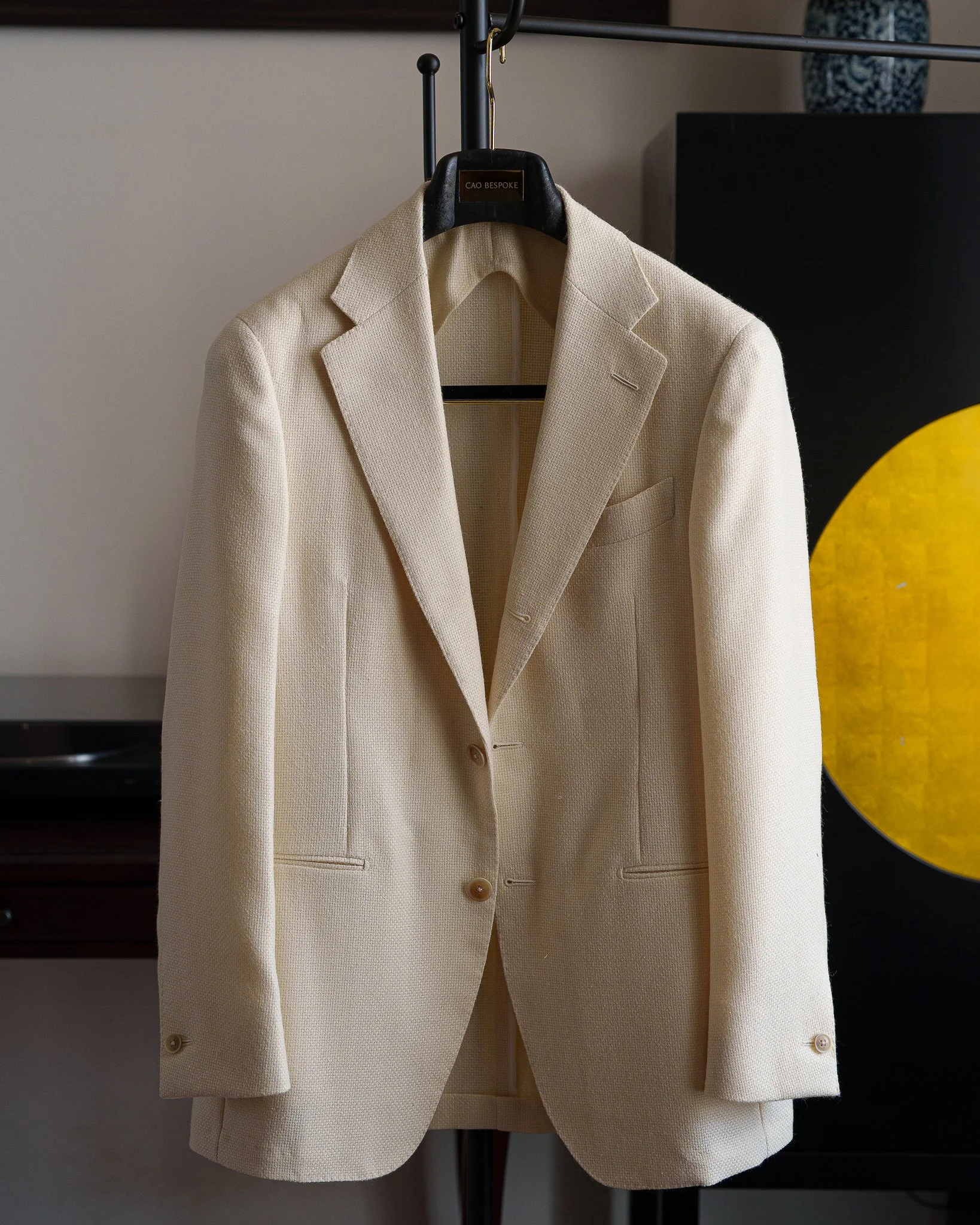 A cream-colored blazer hanging on a black hanger from a metal clothing rack.
