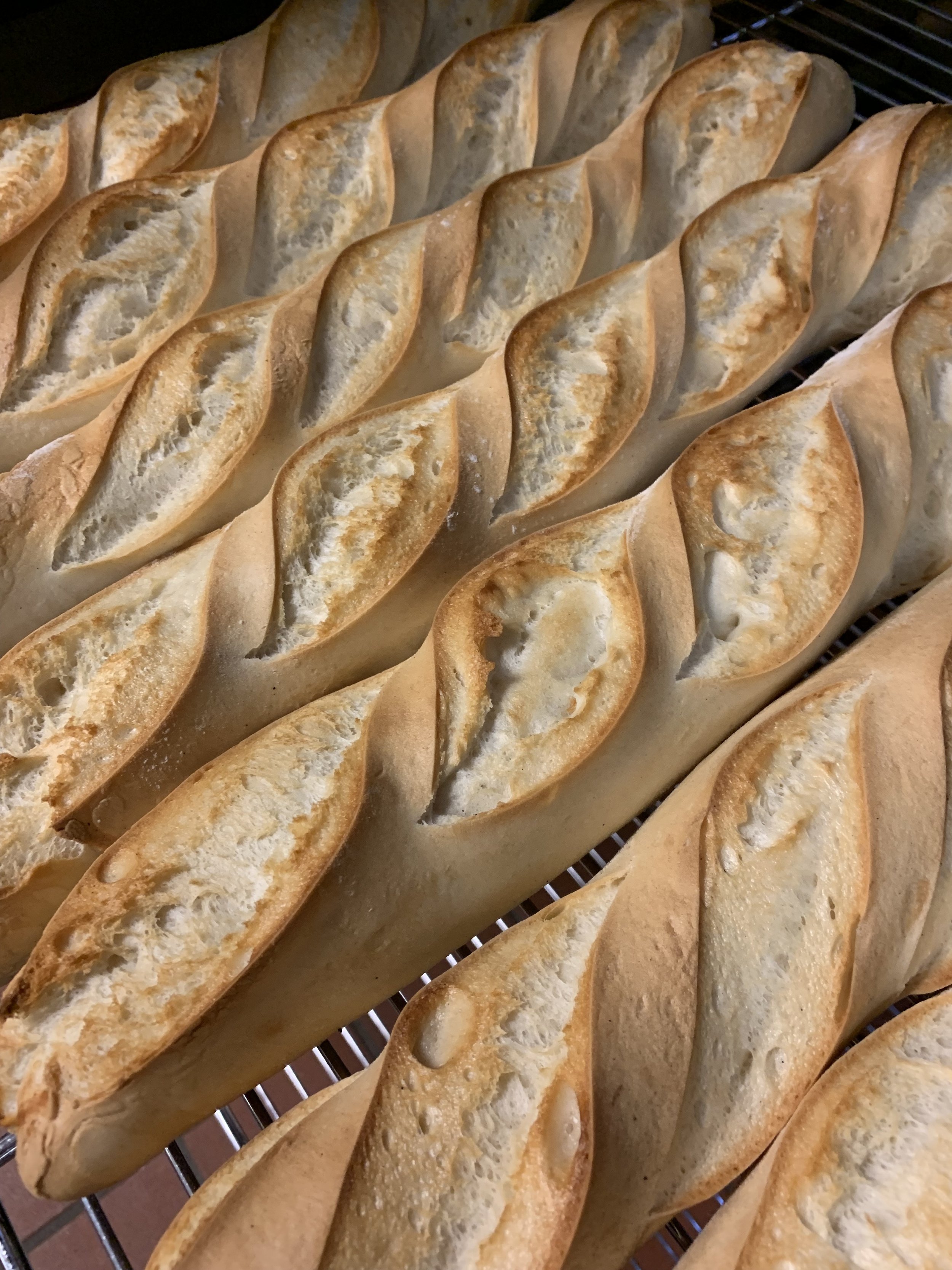 Rows of freshly baked French baguettes cooling on a metal rack.