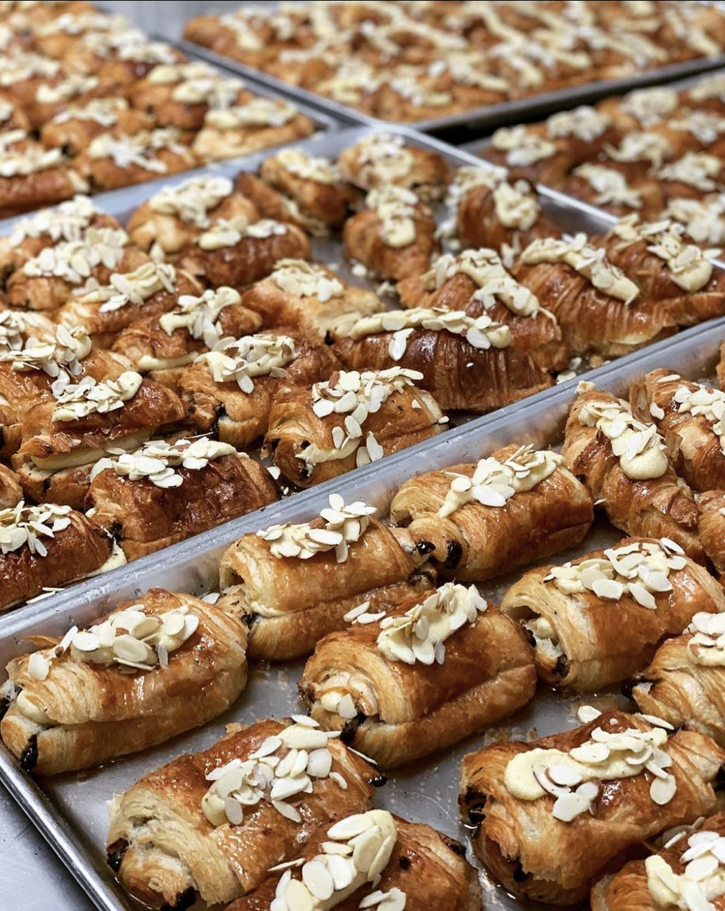 Trays of freshly baked almond croissants topped with sliced almonds.