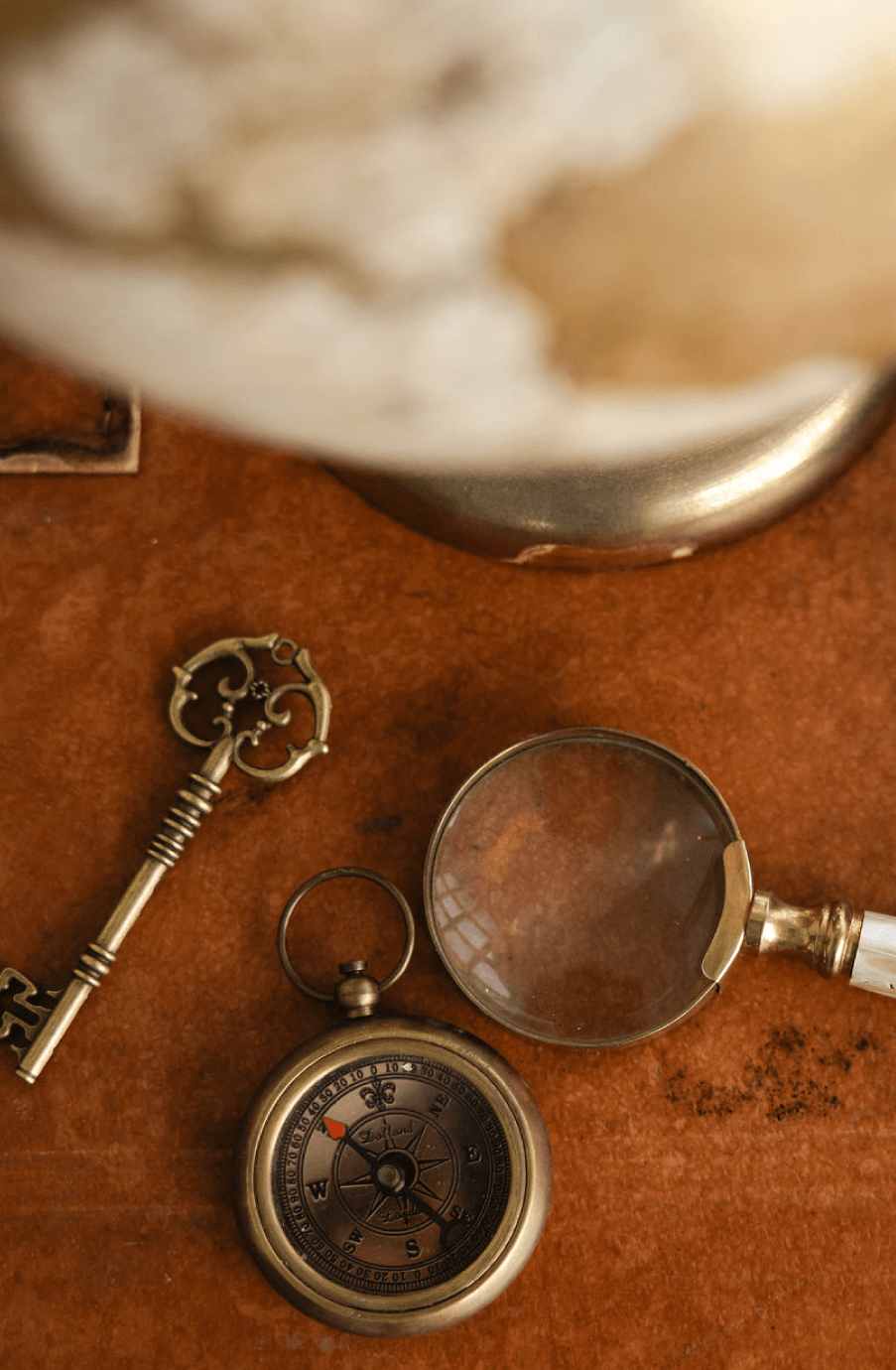 Un llavero en forma de llave antigua, un reloj de brújula, una lupa, y una copa sobre una superficie de madera.