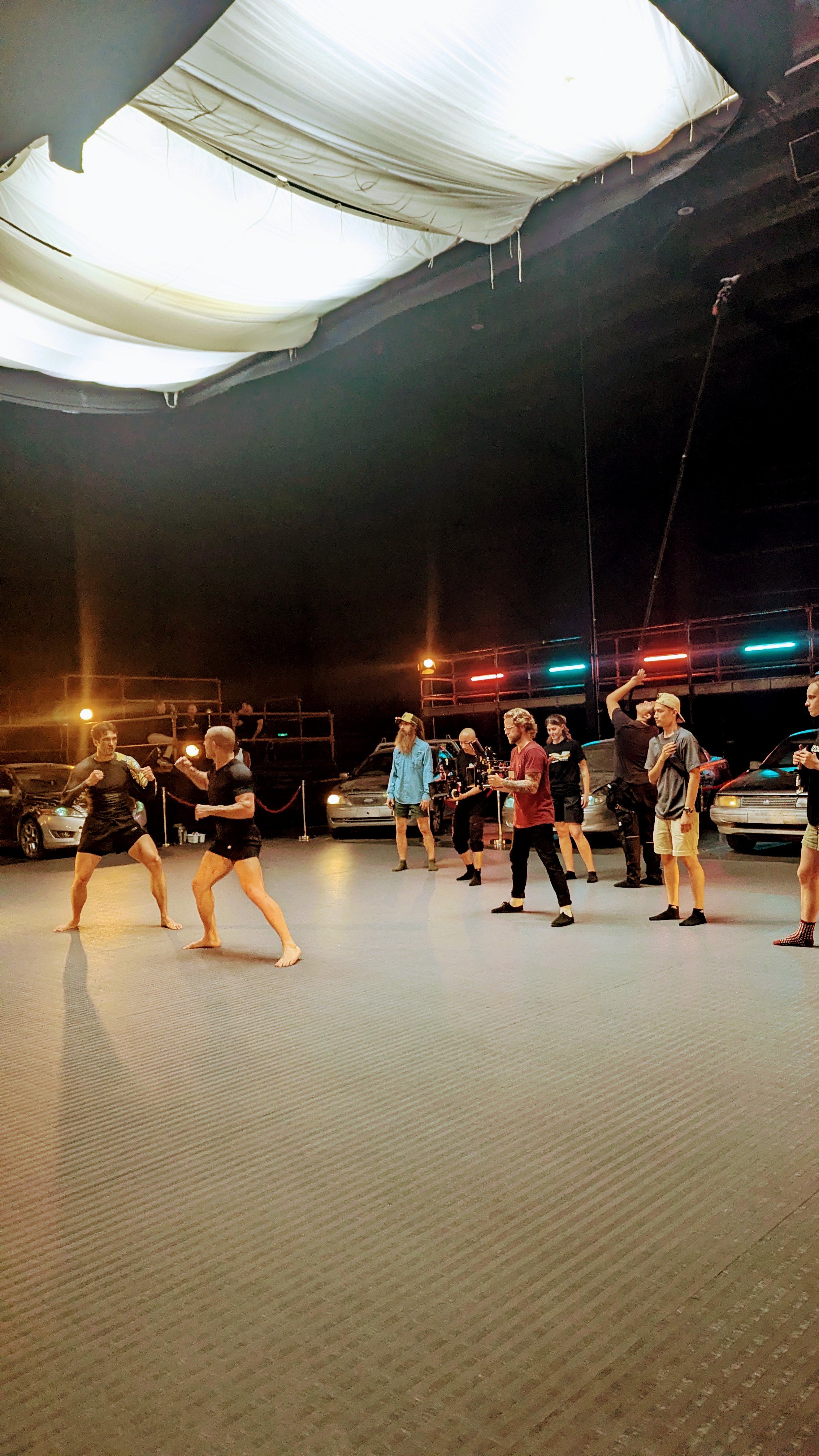 People practicing martial arts in an indoor studio with cars and stage lighting in the background.